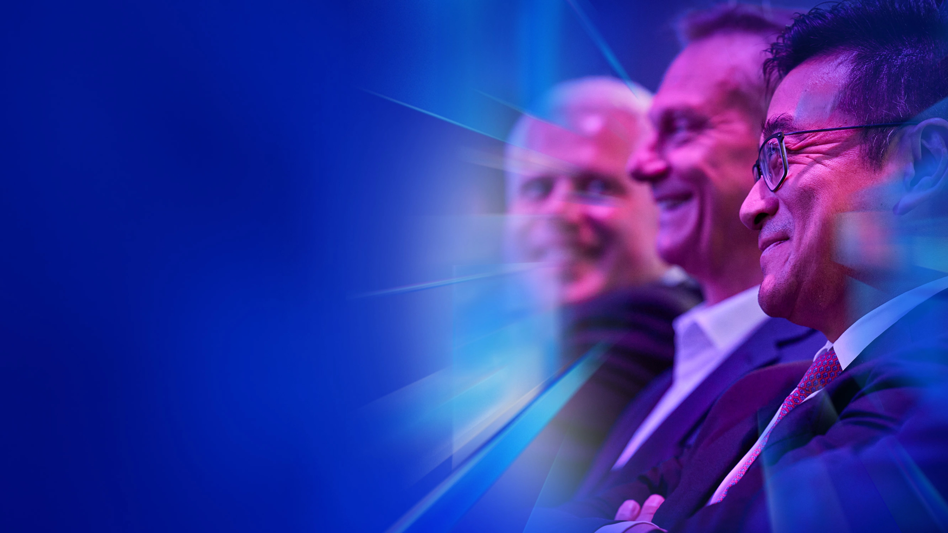 Drei lächelnde Männer im Anzug sitzen beim IAA Summit im Publikum.
