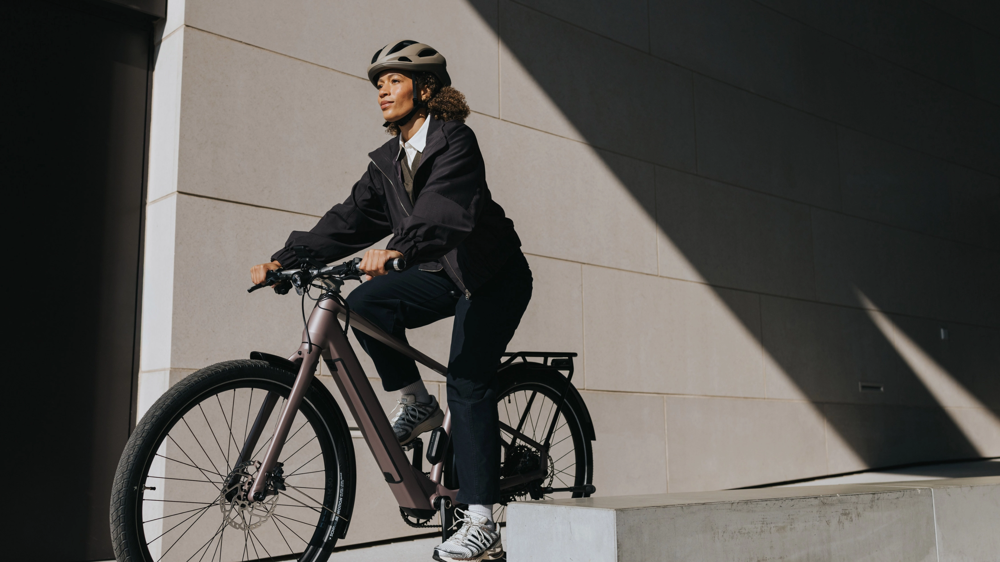 Person mit Helm fährt ein E-Bike neben einem modernen Gebäude.