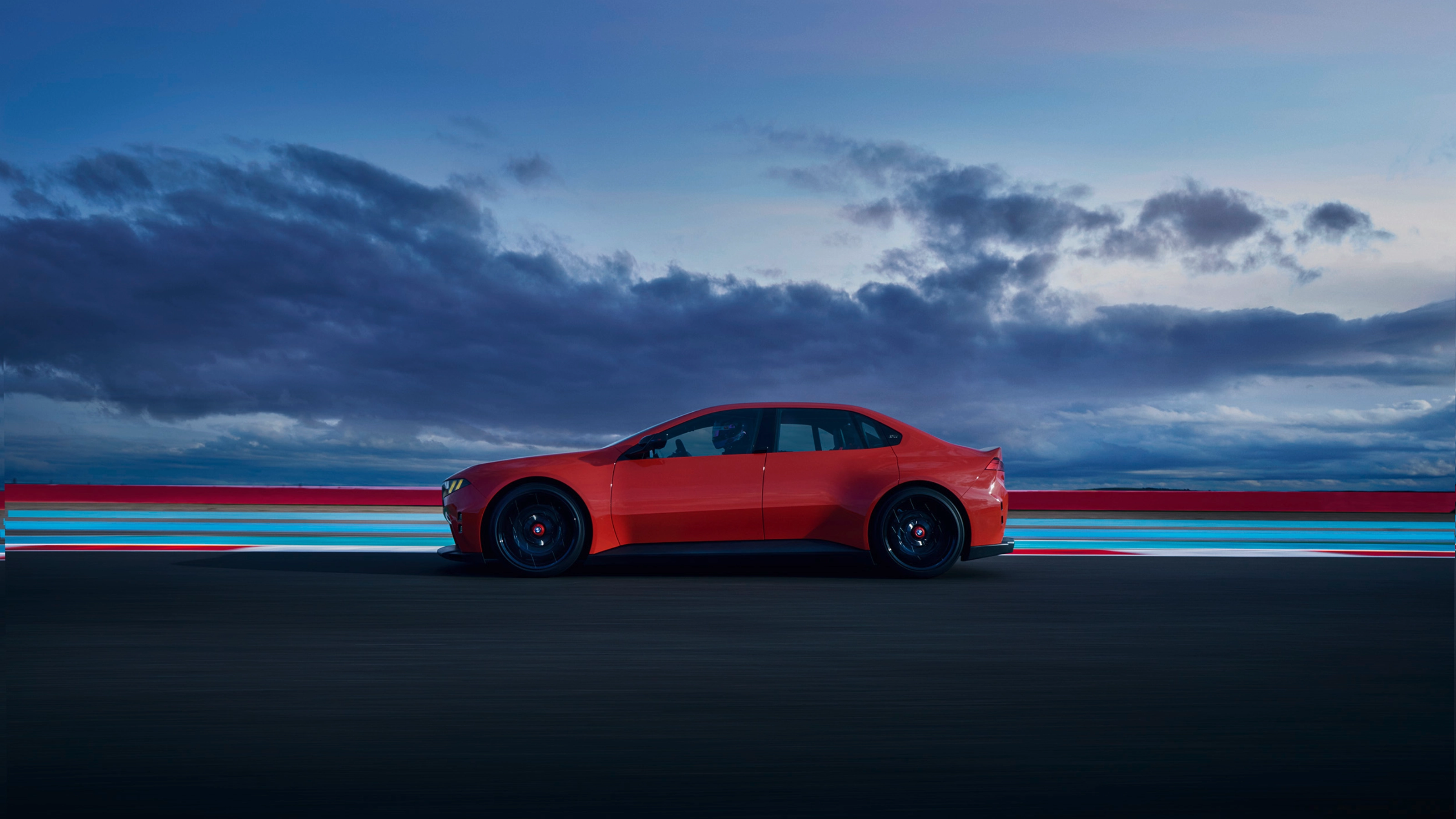 Red car driving on a road at dusk with clouds in the background.