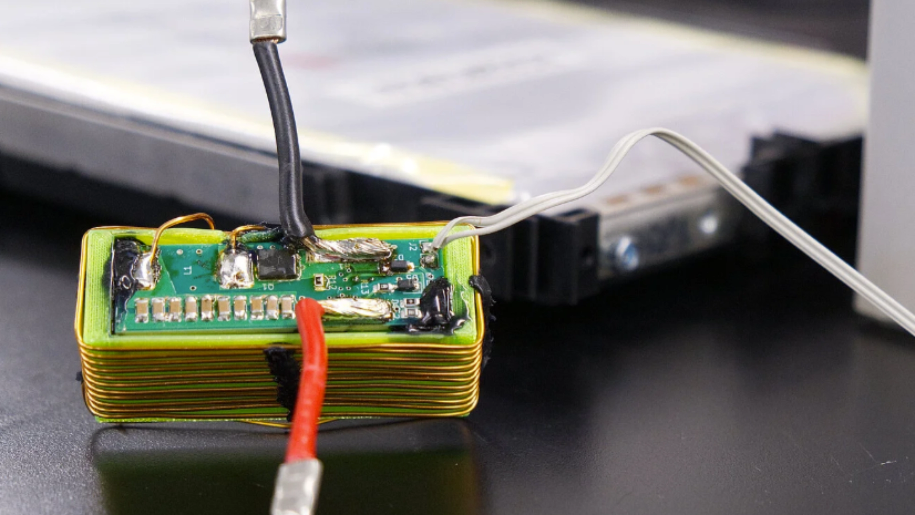 Nahaufnahme eines elektronischen Batteriemoduls mit angeschlossenen Kabeln auf einem Labortisch.