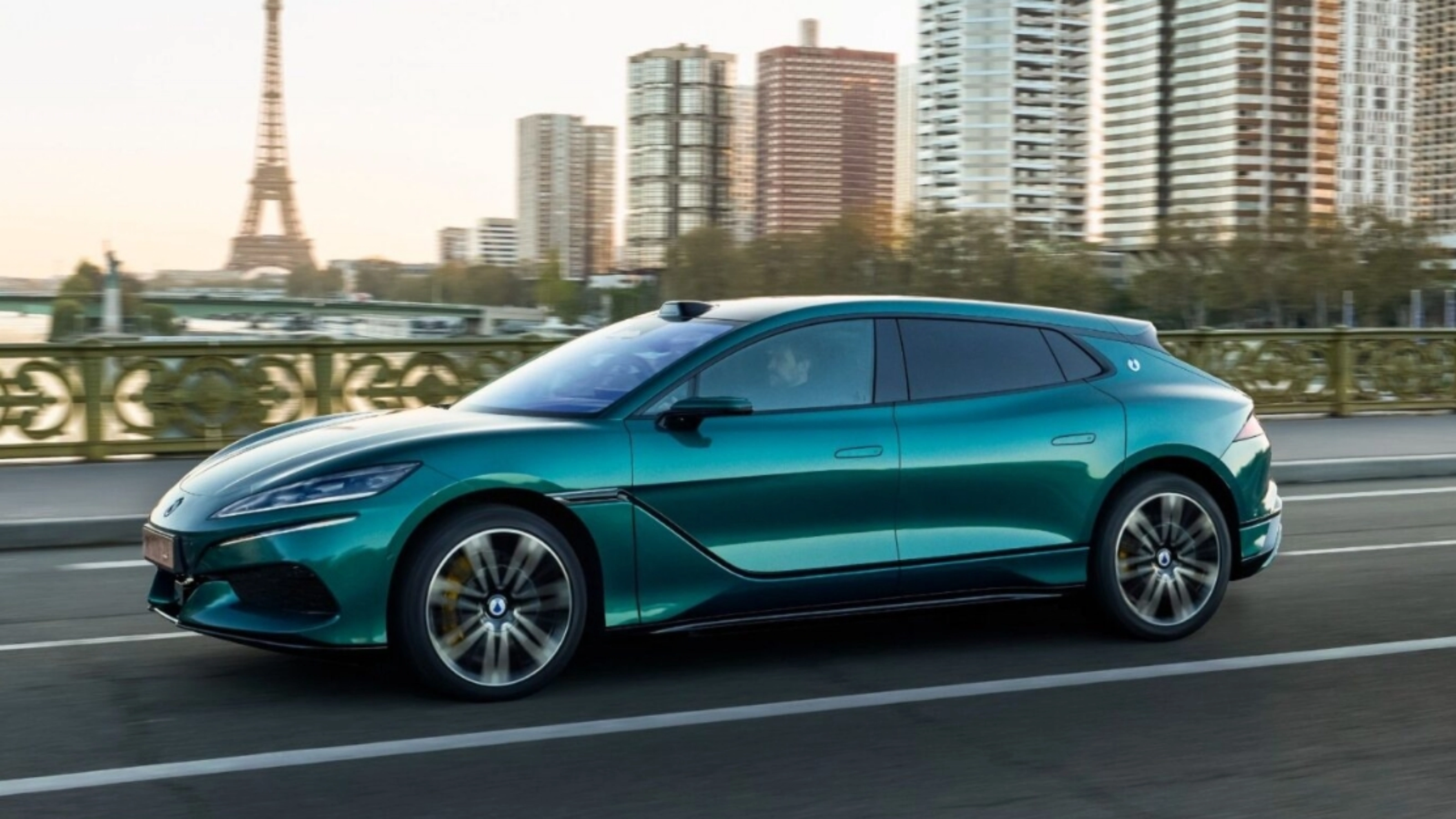 Turquoise BYD electric car driving on a city road with a skyline in the background.