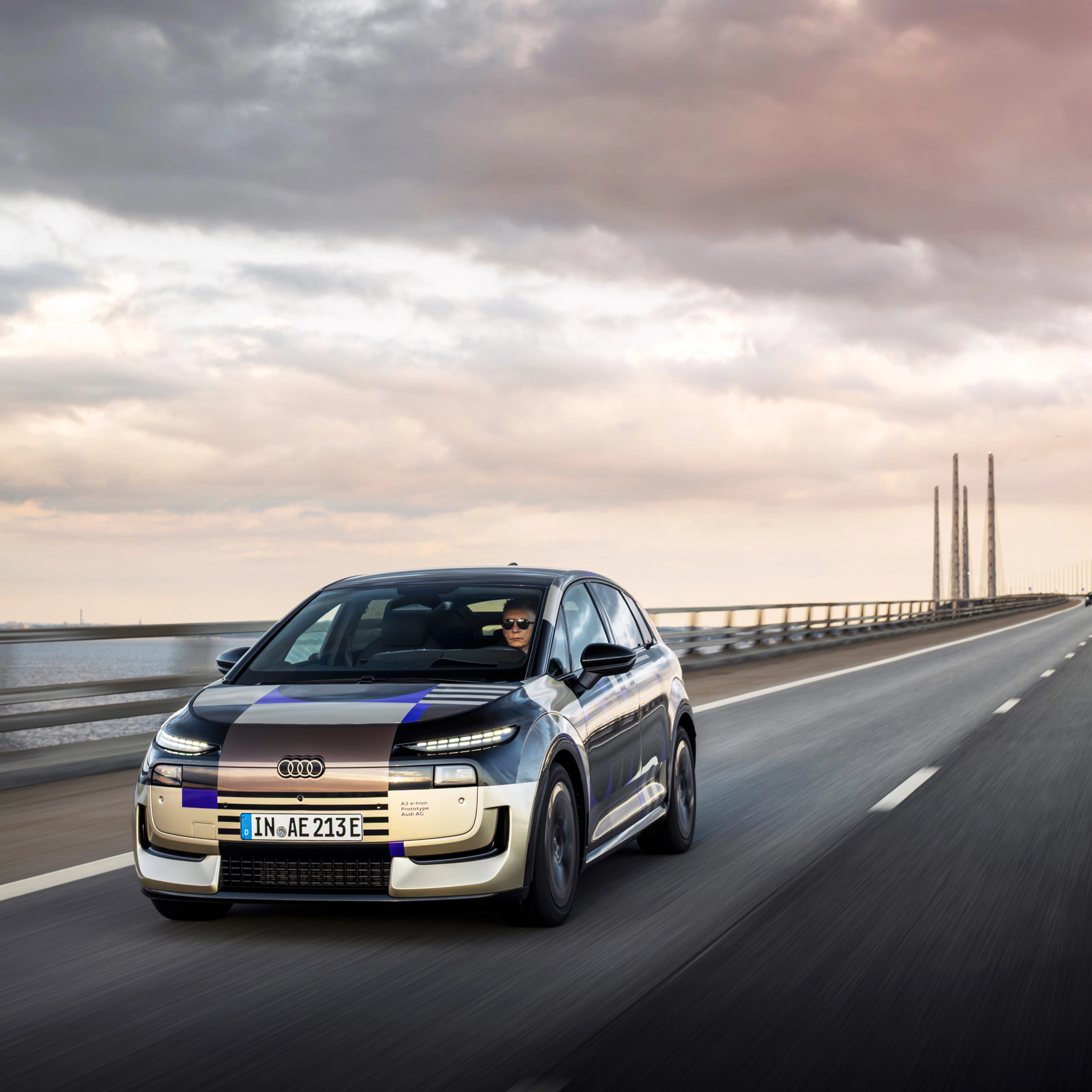 Audi prototype electric vehicle driving on an open road at sunset.