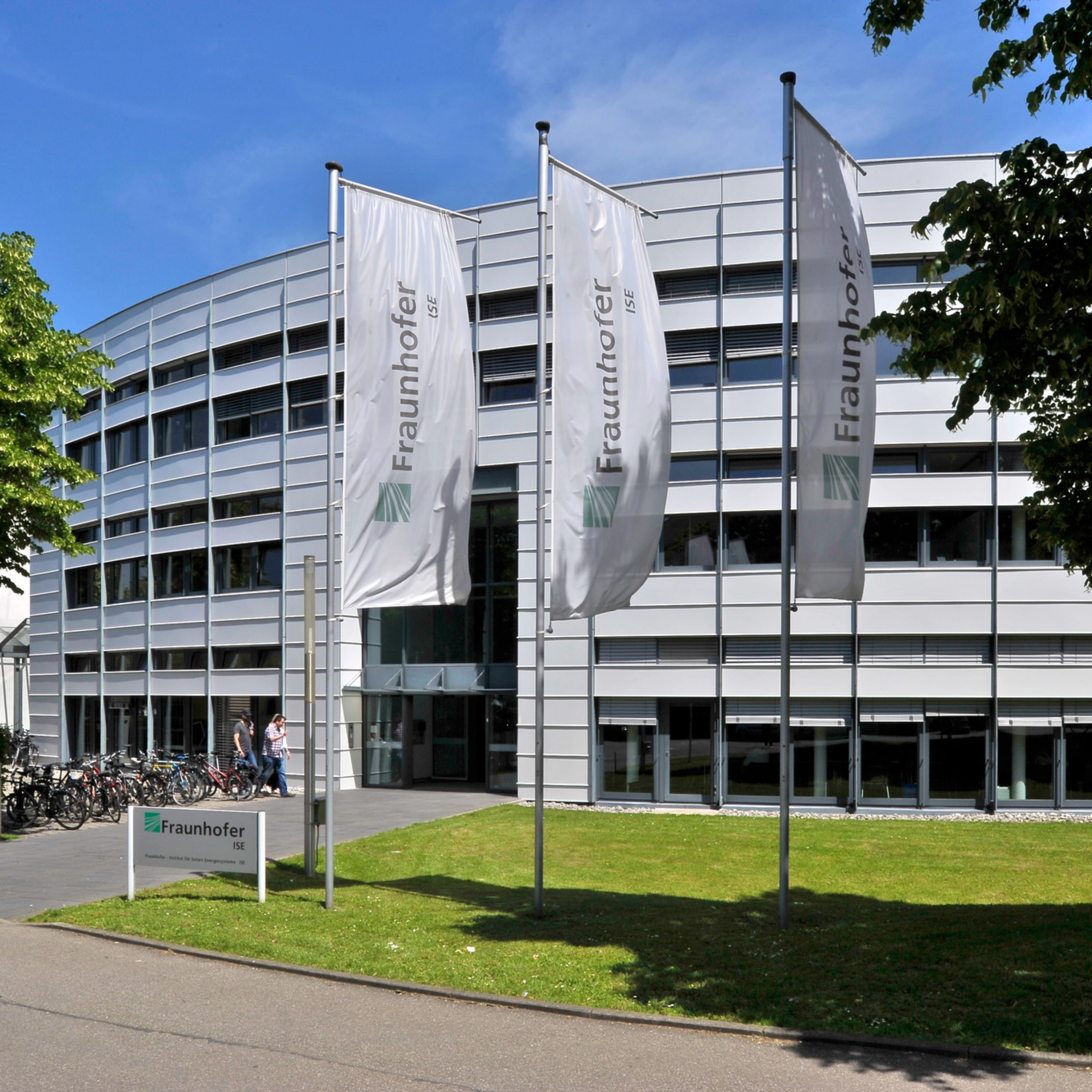 Modernes Fraunhofer-Institutsgebäude mit Fahnen und Bäumen davor.