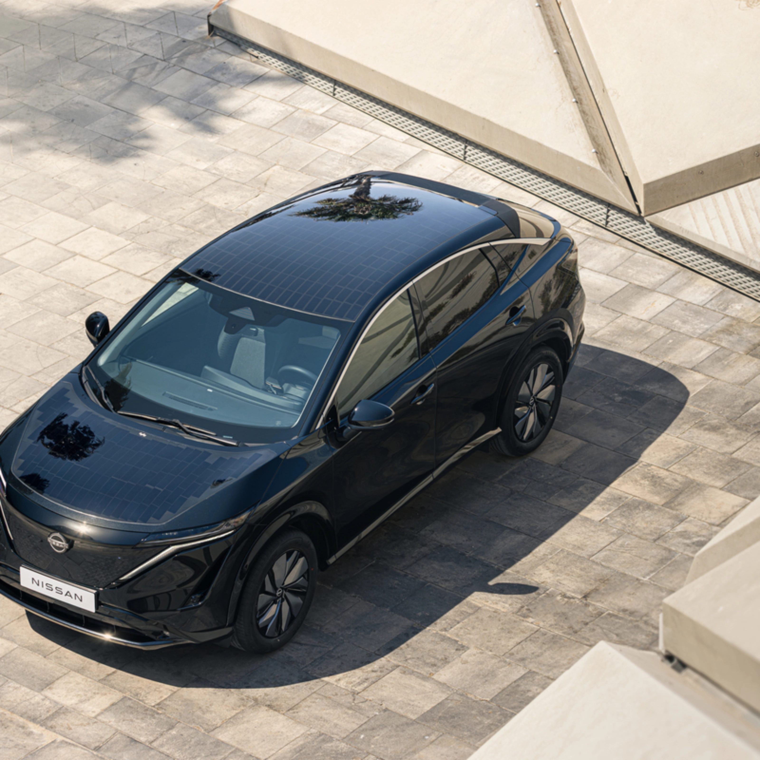 Ein schwarzes Elektro-SUV von Nissan steht auf einer gepflasterten Fläche im Sonnenlicht.