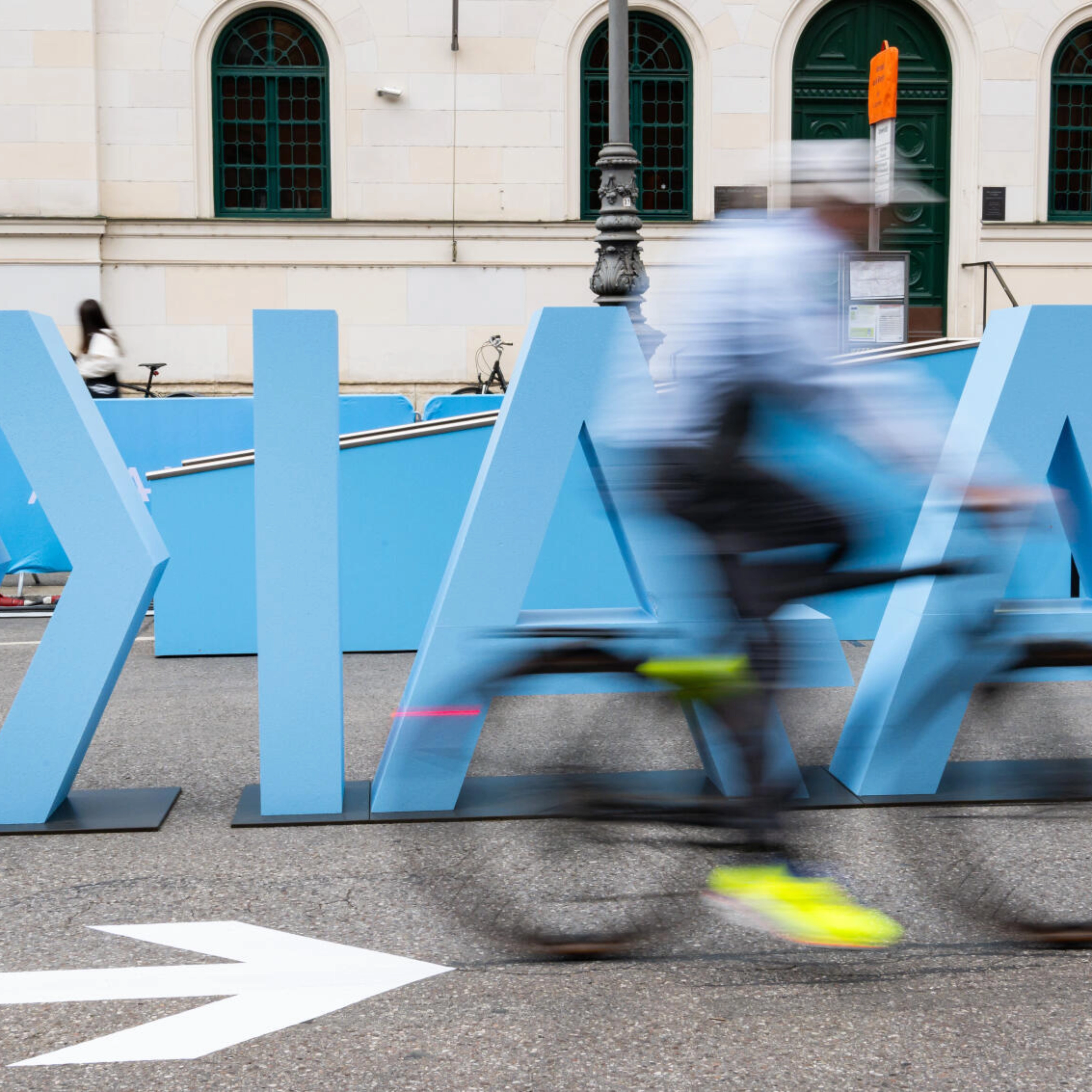 Cyclist rides past large IAA Mobility lettering on a city street.
