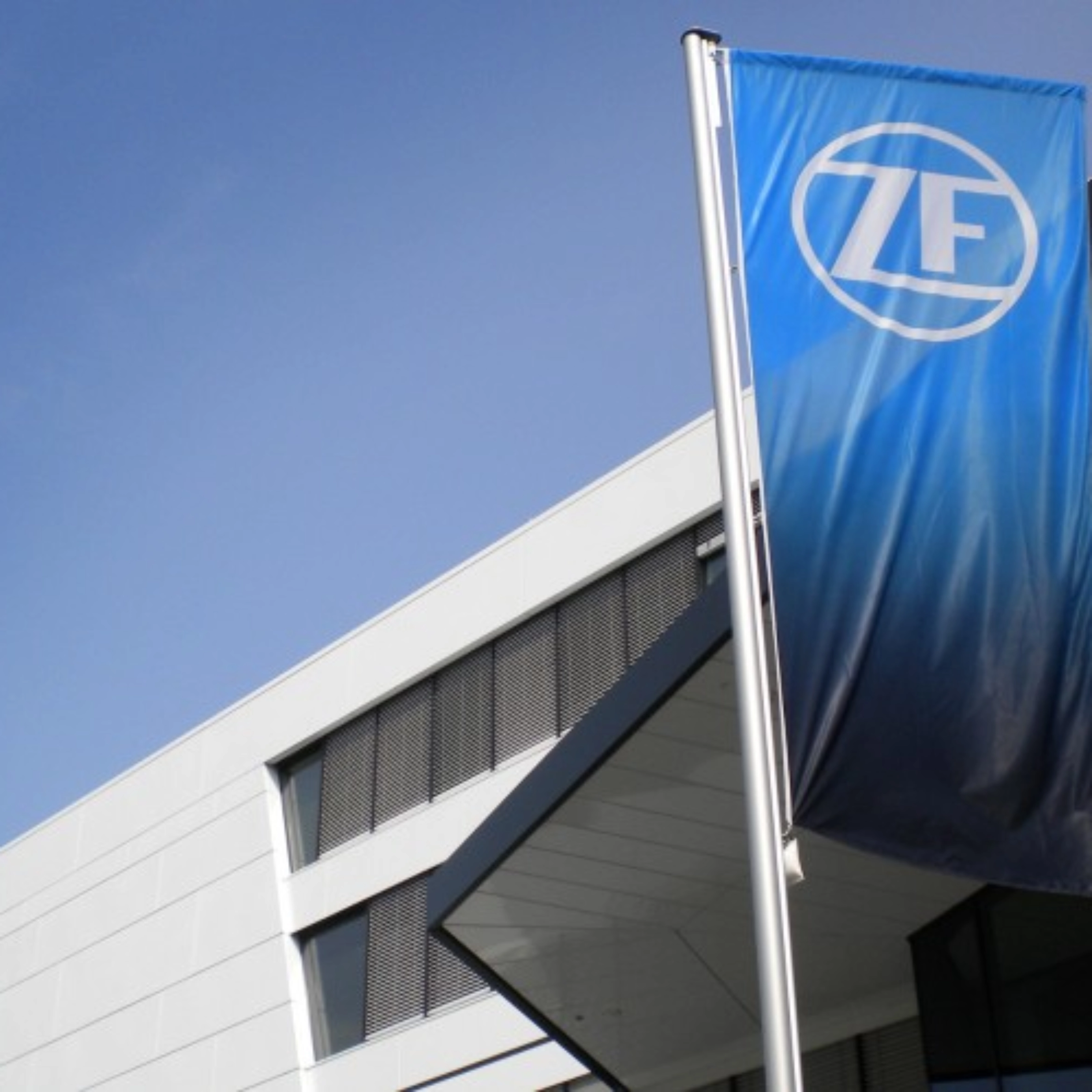 Blaue ZF-Flagge vor einem modernen Bürogebäude mit weißer Fassade.