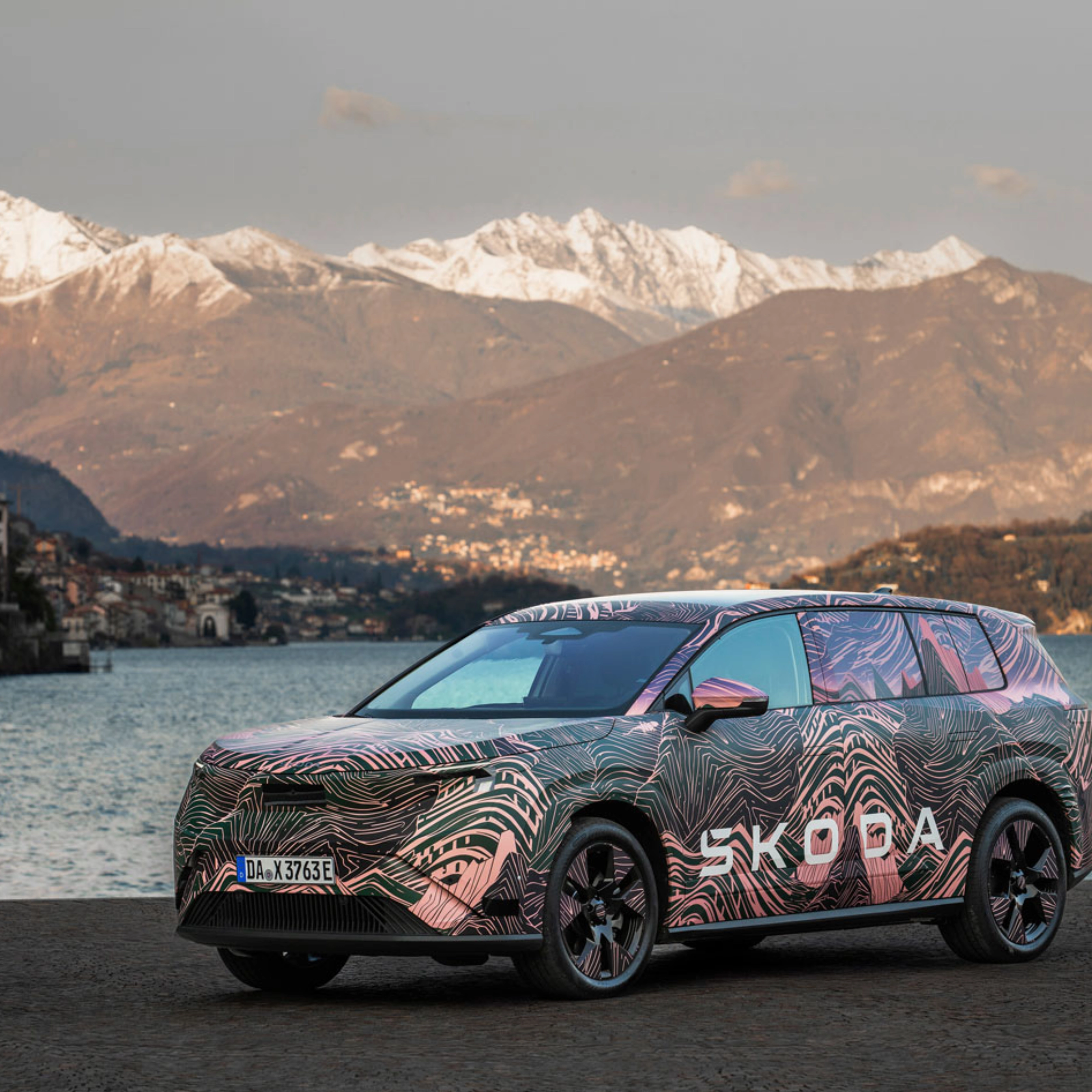 Getarnter Škoda steht am See vor schneebedeckten Bergen.