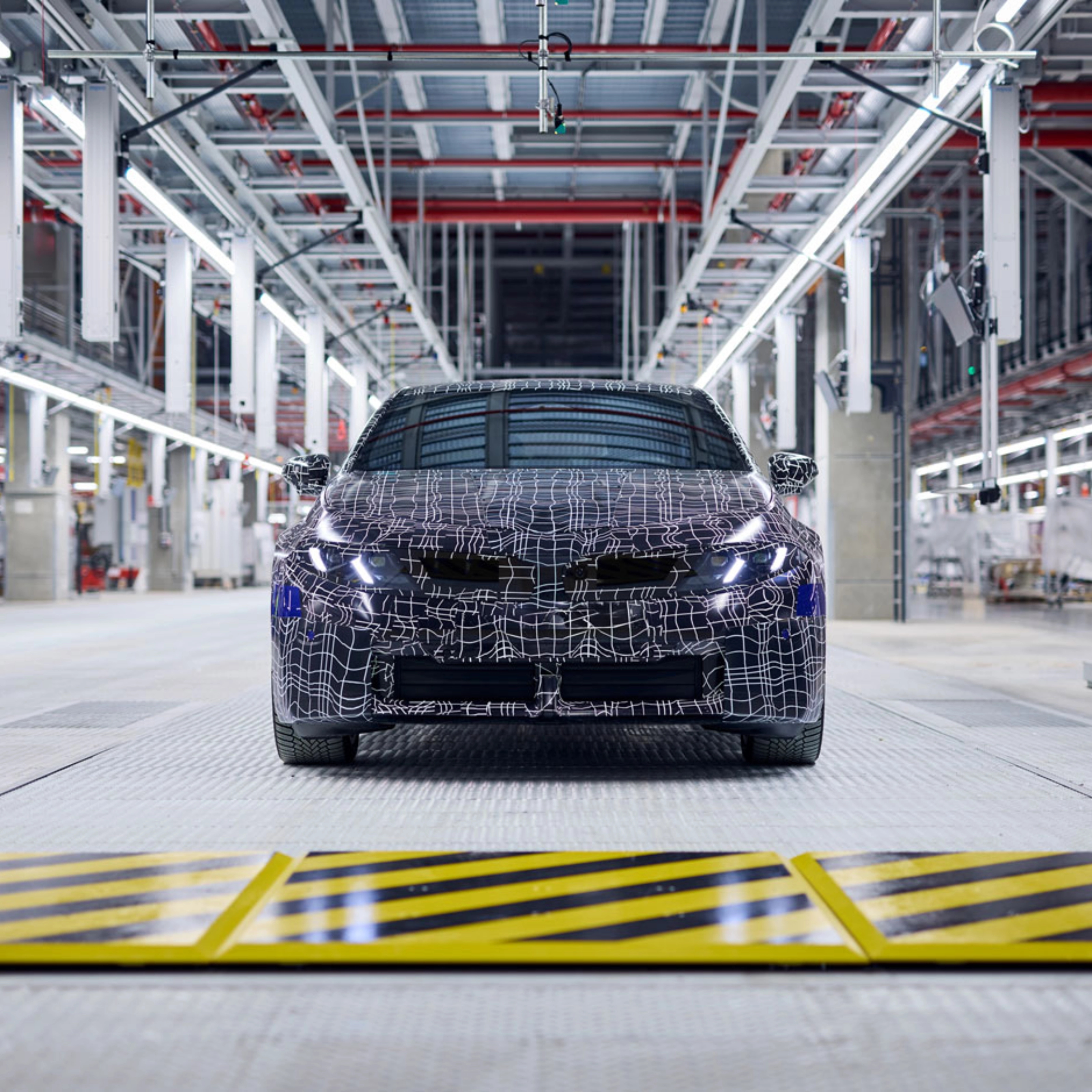 Ein getarntes Auto-Prototyp steht in einer hell beleuchteten Fahrzeugproduktionshalle.