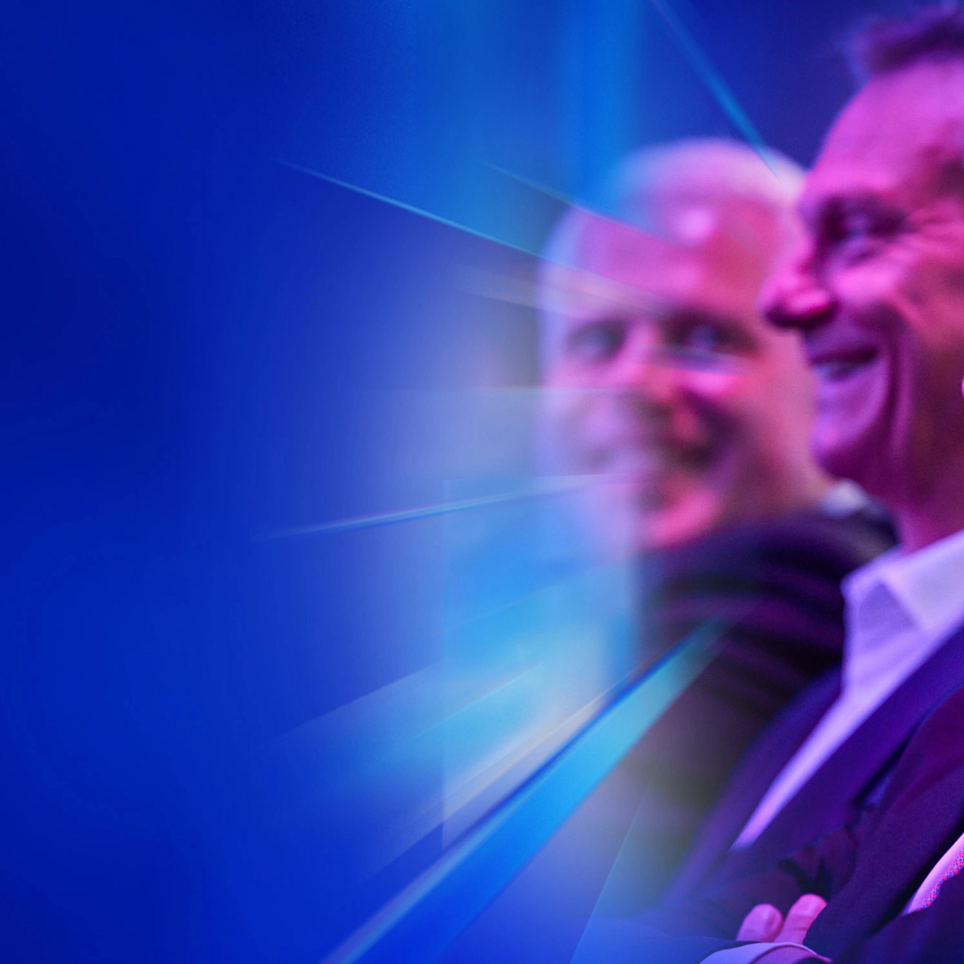 Drei lächelnde Männer im Anzug sitzen beim IAA Summit im Publikum.