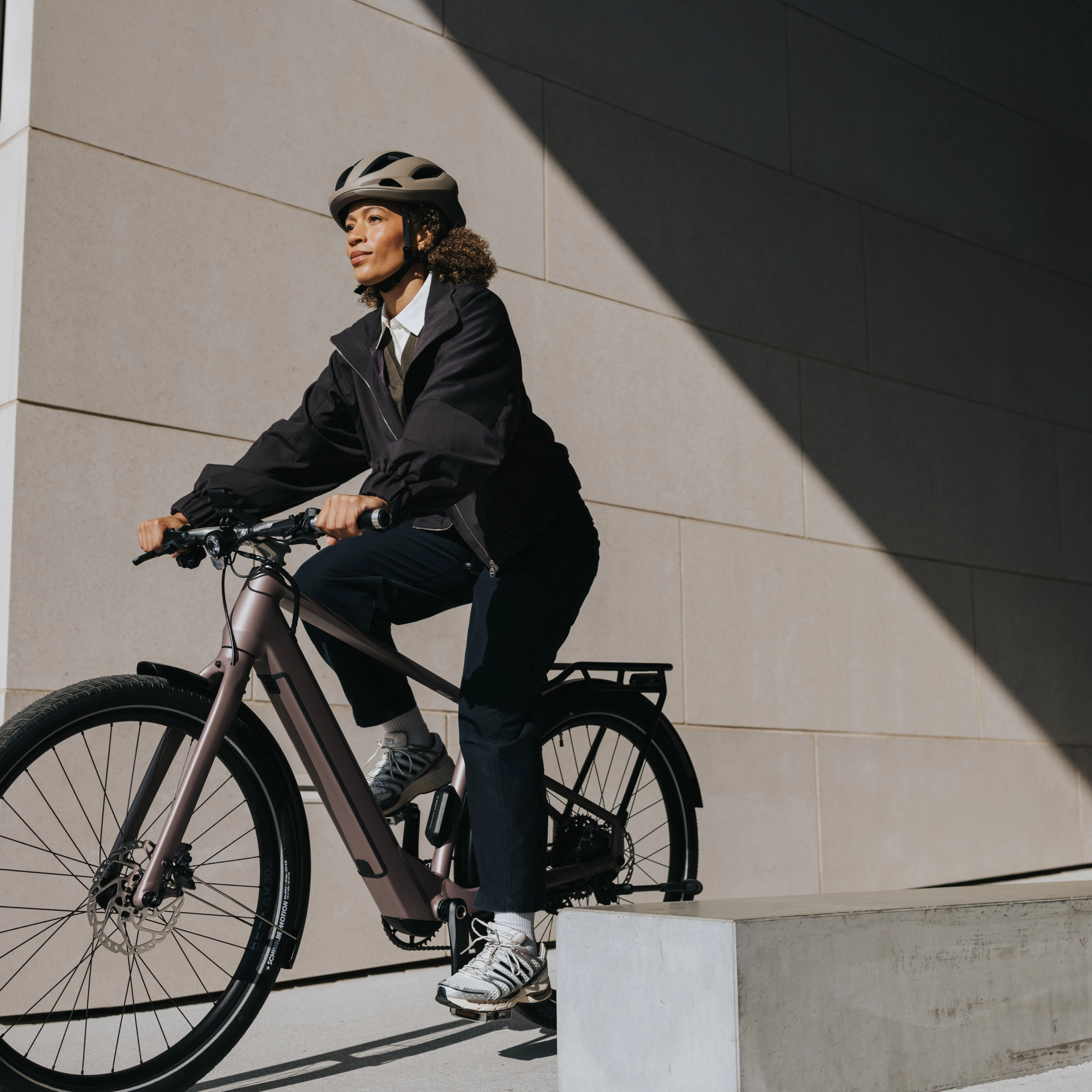 Person mit Helm fährt ein E-Bike neben einem modernen Gebäude.