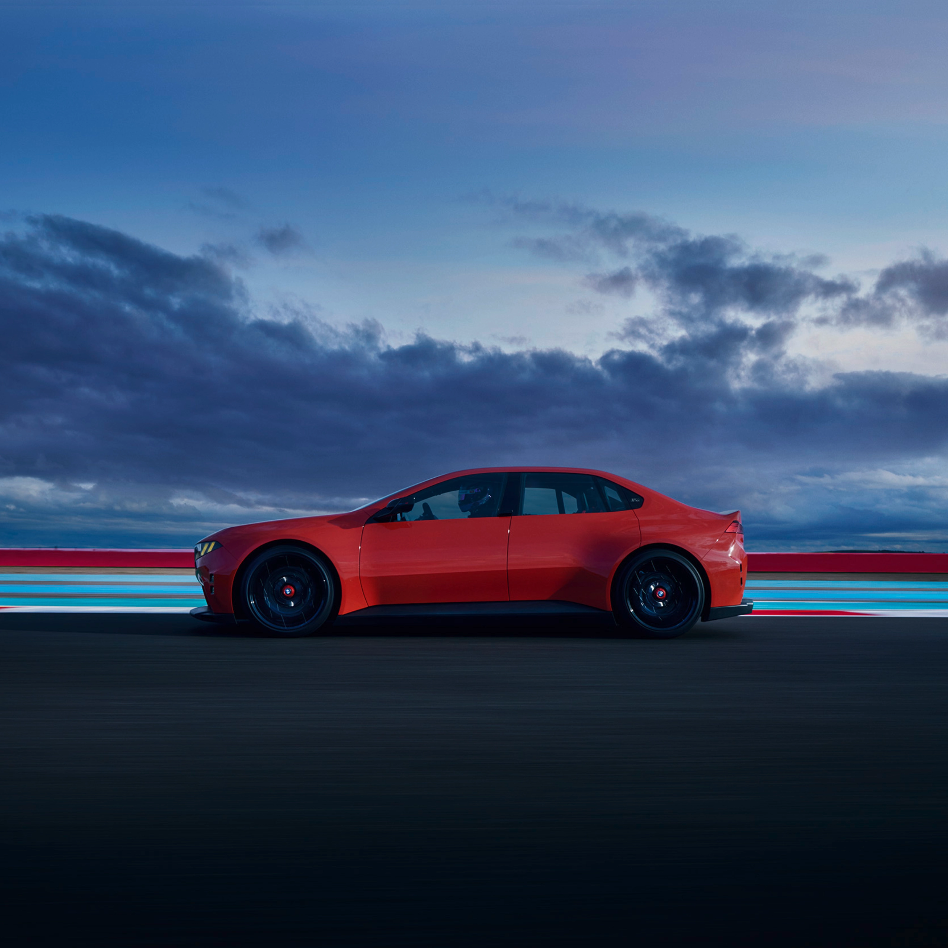 Red car driving on a road at dusk with clouds in the background.