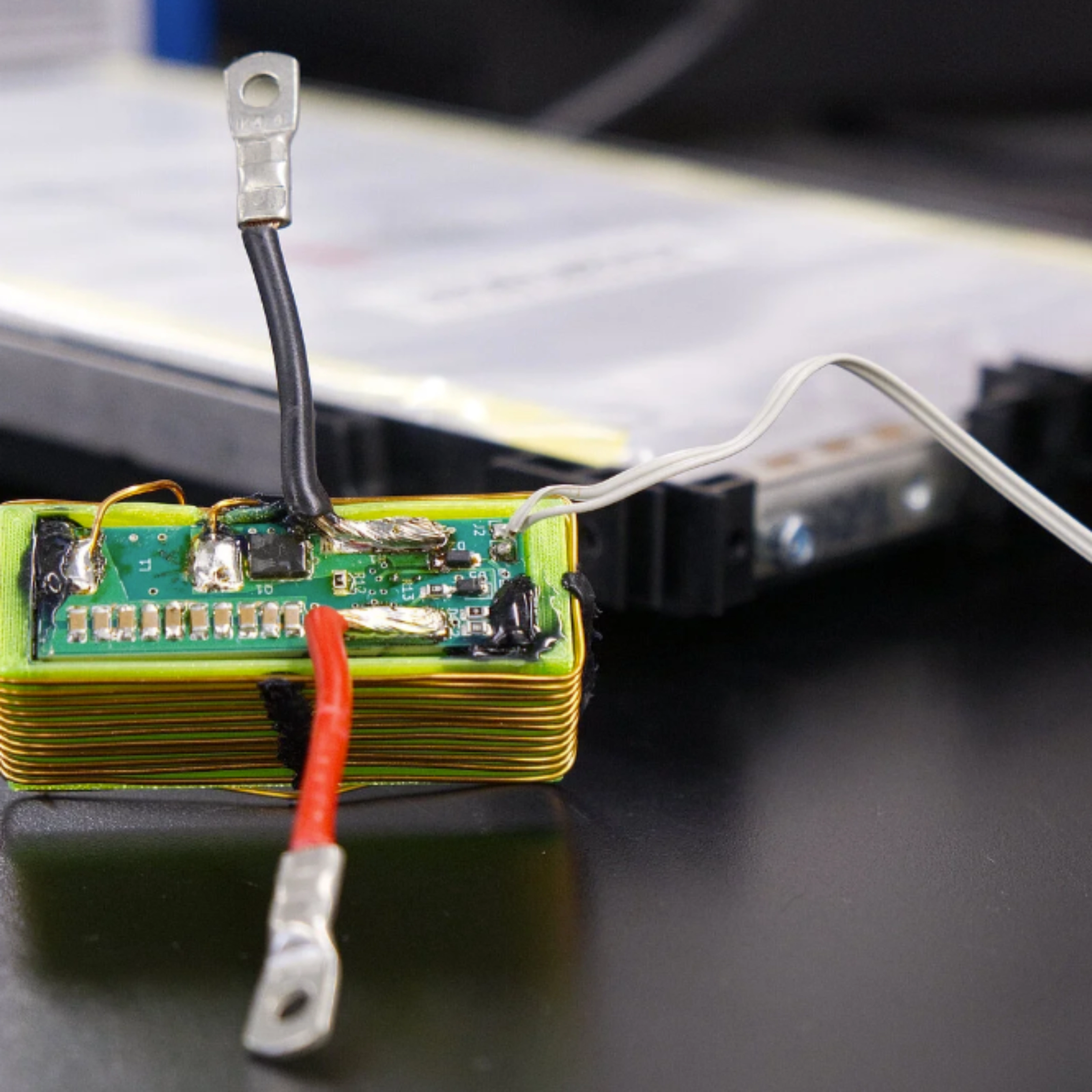 Nahaufnahme eines elektronischen Batteriemoduls mit angeschlossenen Kabeln auf einem Labortisch.