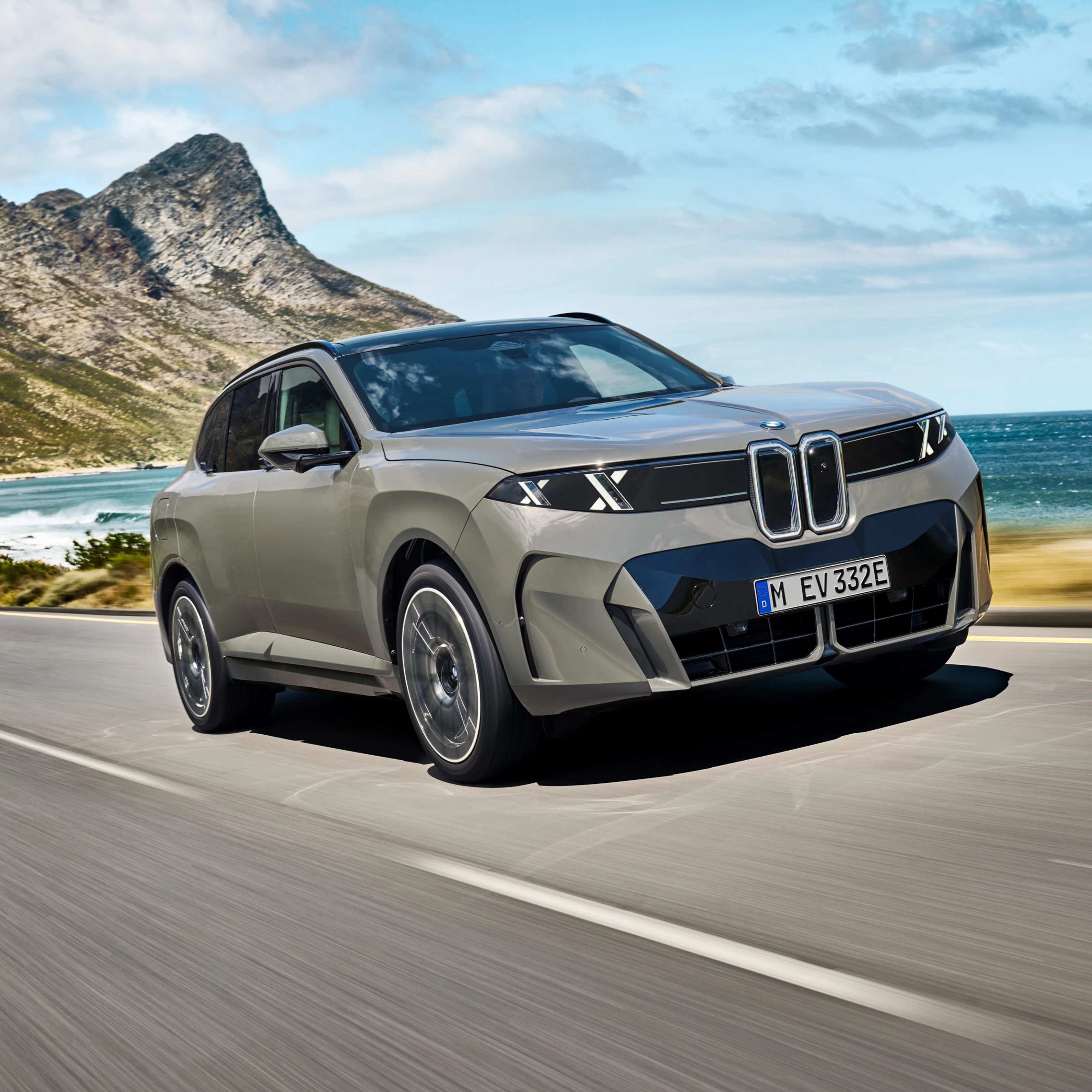 BMW SUV fährt auf einer Küstenstraße mit Bergen und Meer im Hintergrund.