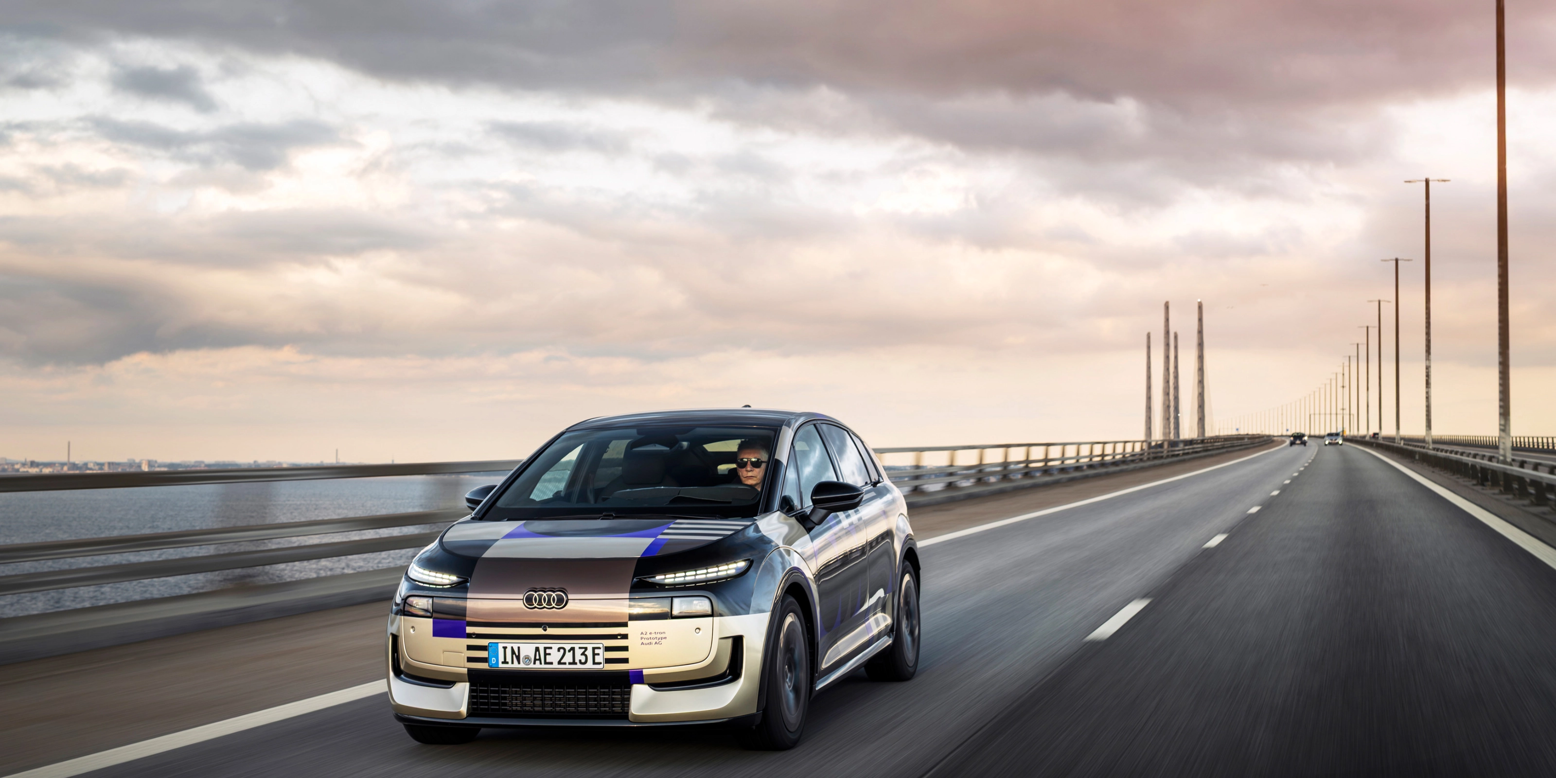Audi prototype electric vehicle driving on an open road at sunset.