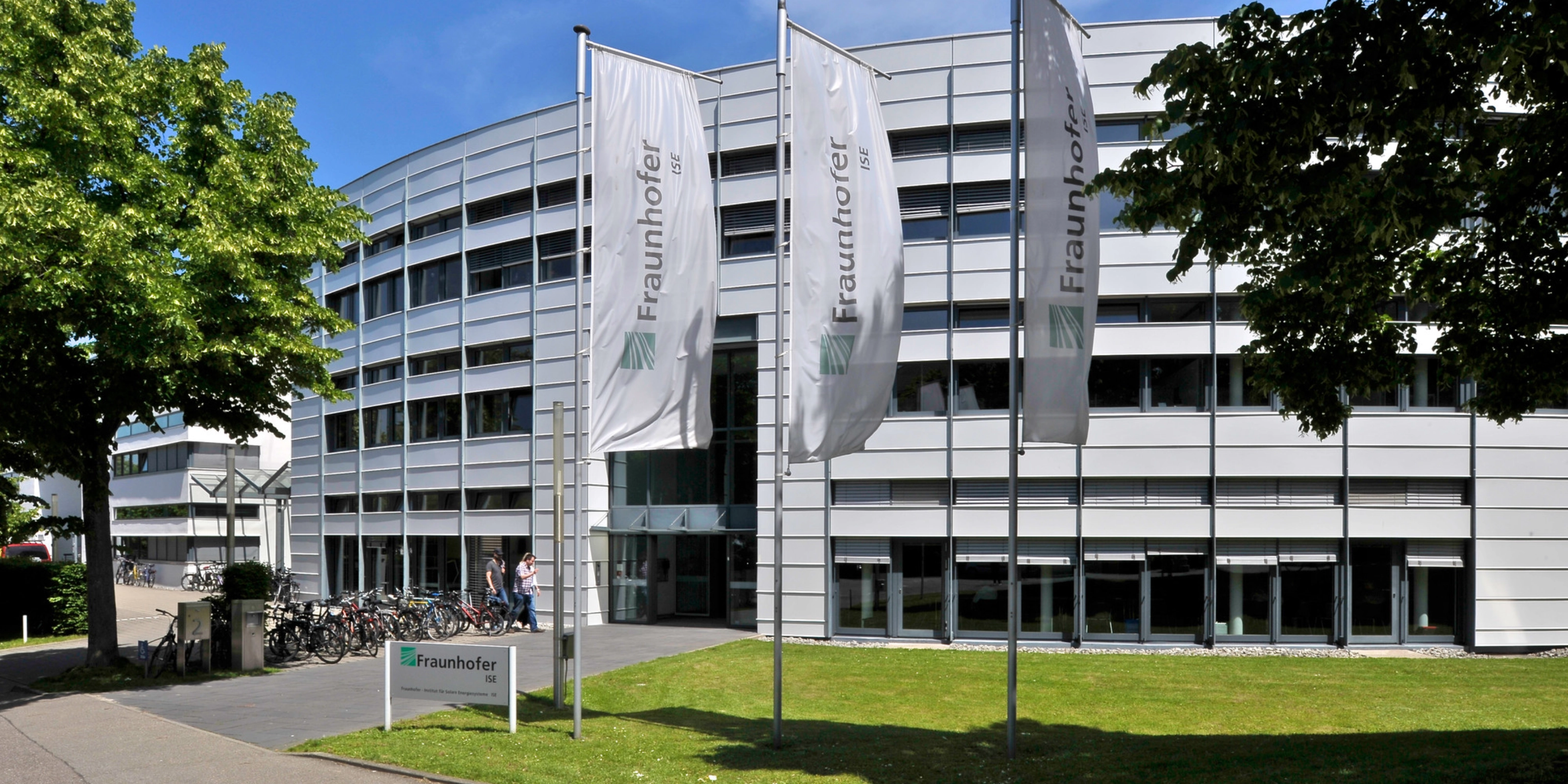 Modernes Fraunhofer-Institutsgebäude mit Fahnen und Bäumen davor.