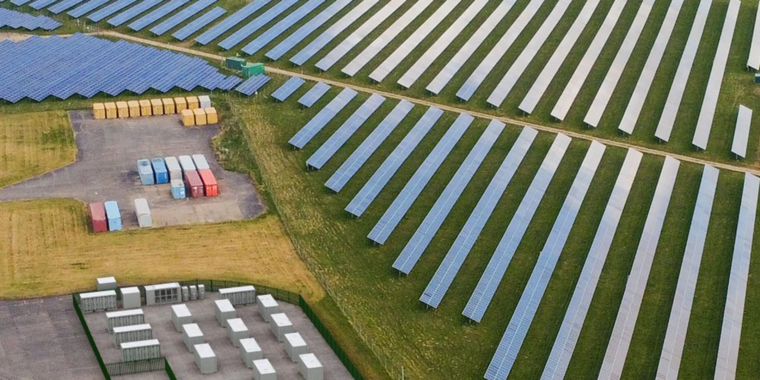 Luftaufnahme einer Solaranlage mit Reihen von Solarpaneelen und mehreren Containern.