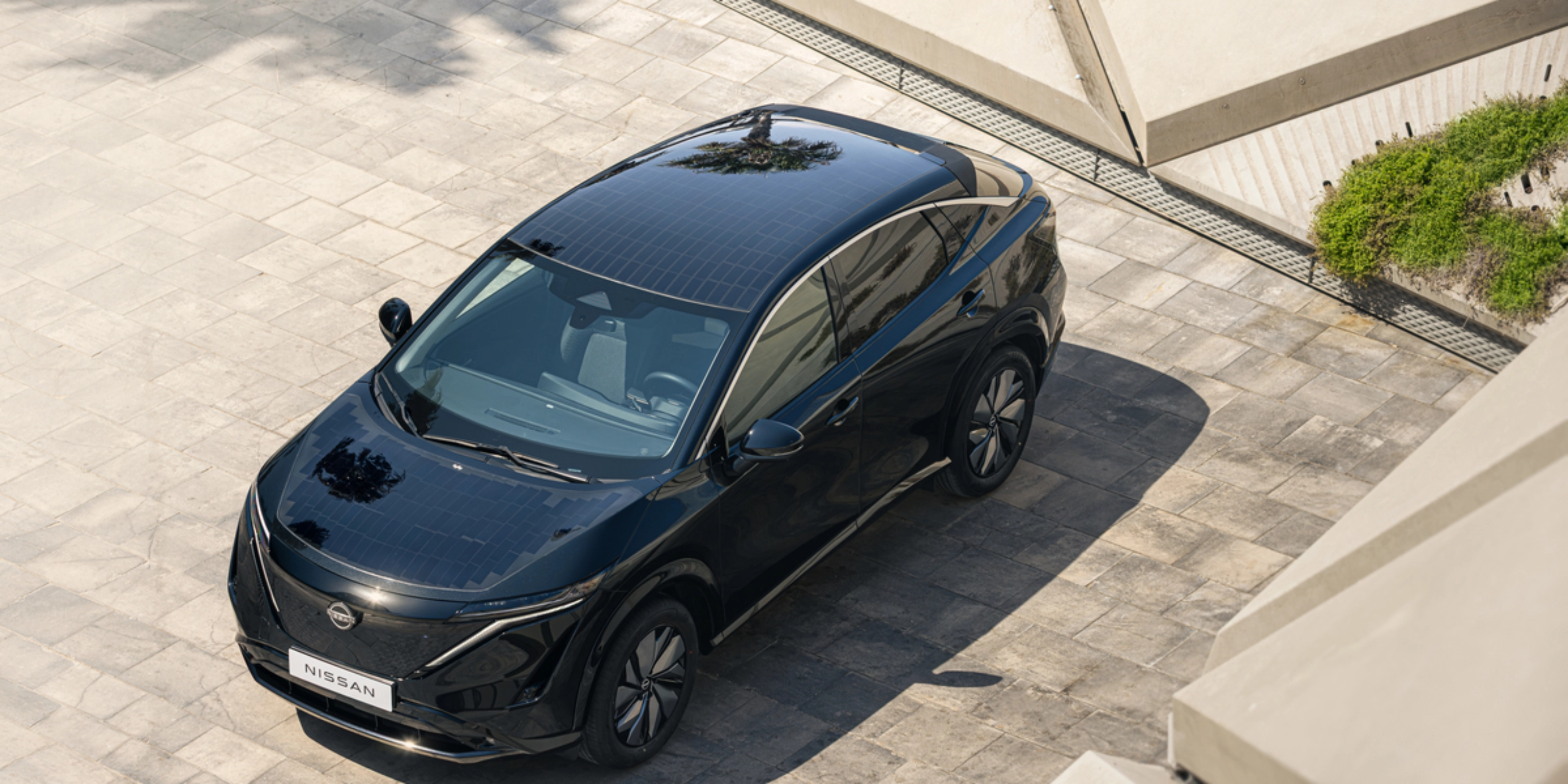 Ein schwarzes Elektro-SUV von Nissan steht auf einer gepflasterten Fläche im Sonnenlicht.