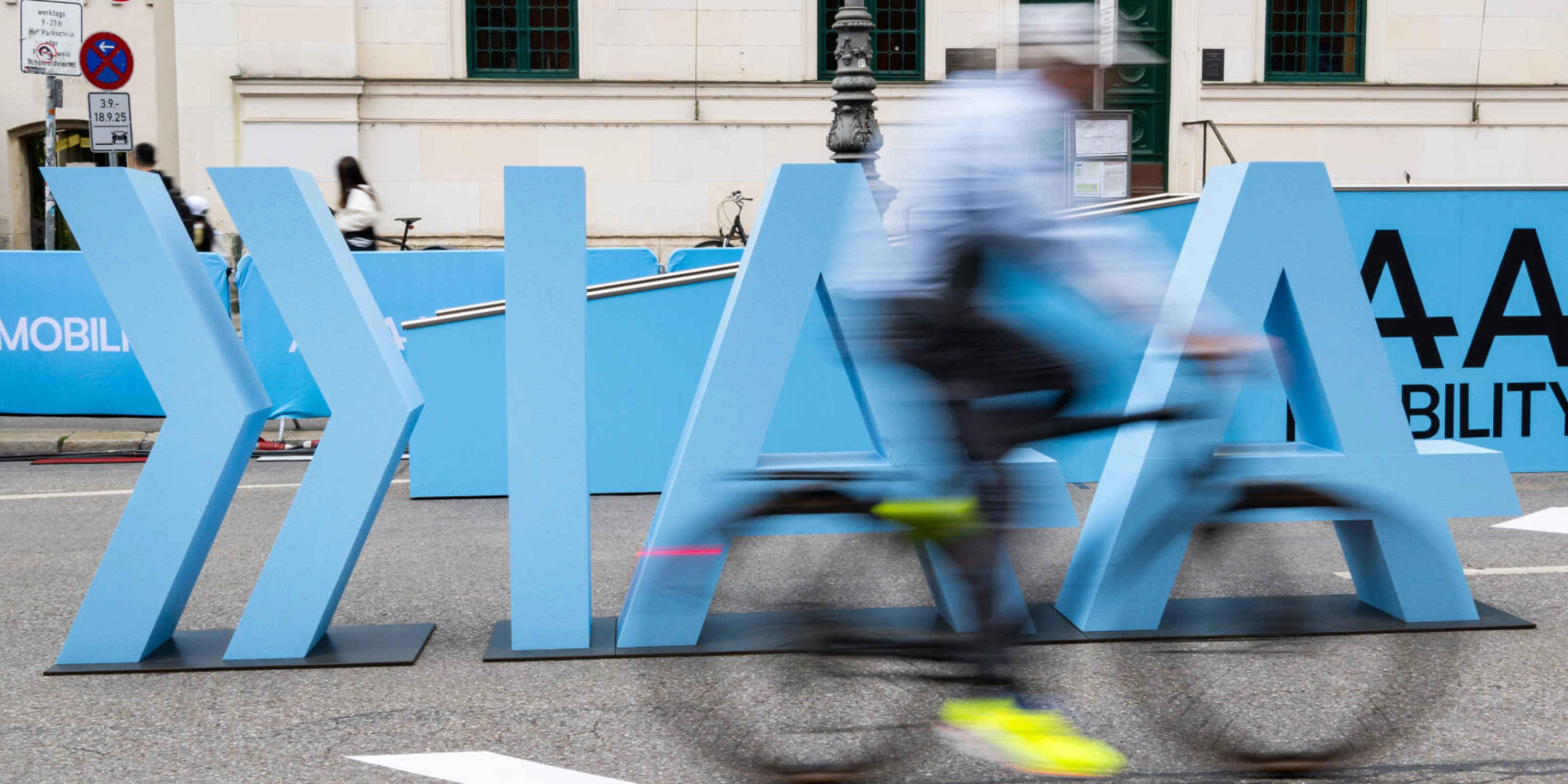 Cyclist rides past large IAA Mobility lettering on a city street.