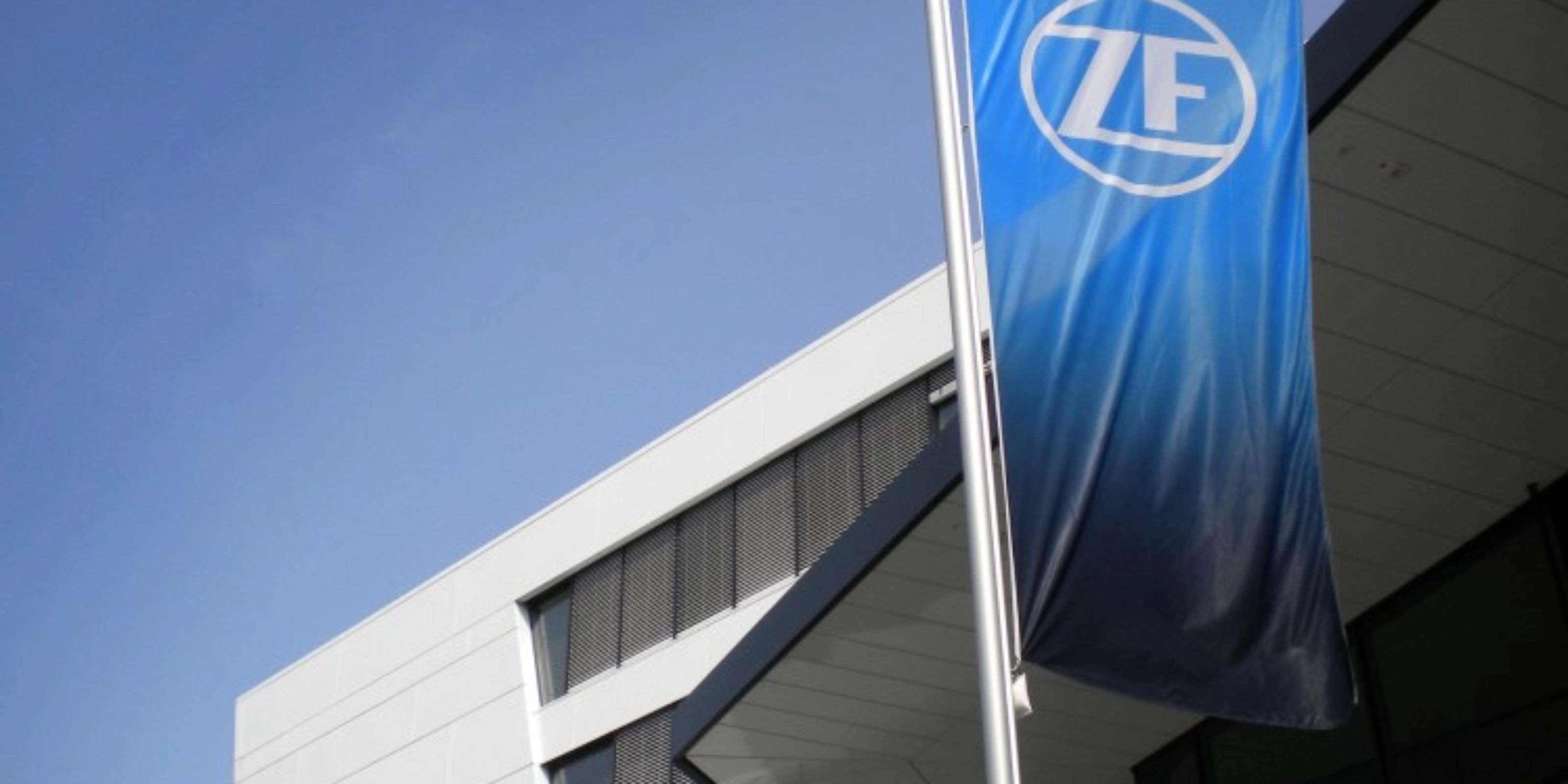 Blaue ZF-Flagge vor einem modernen Bürogebäude mit weißer Fassade.