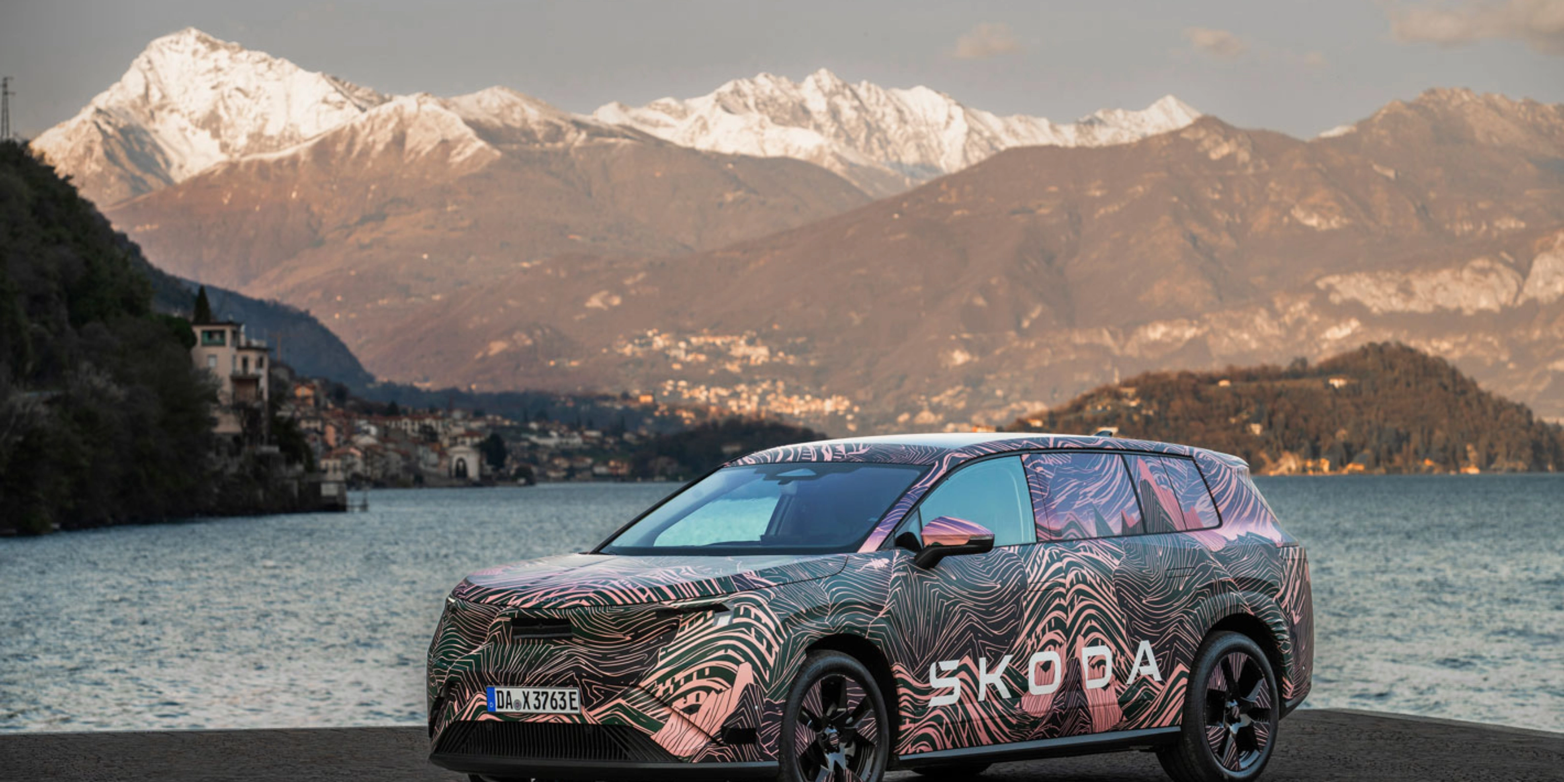 Getarnter Škoda steht am See vor schneebedeckten Bergen.
