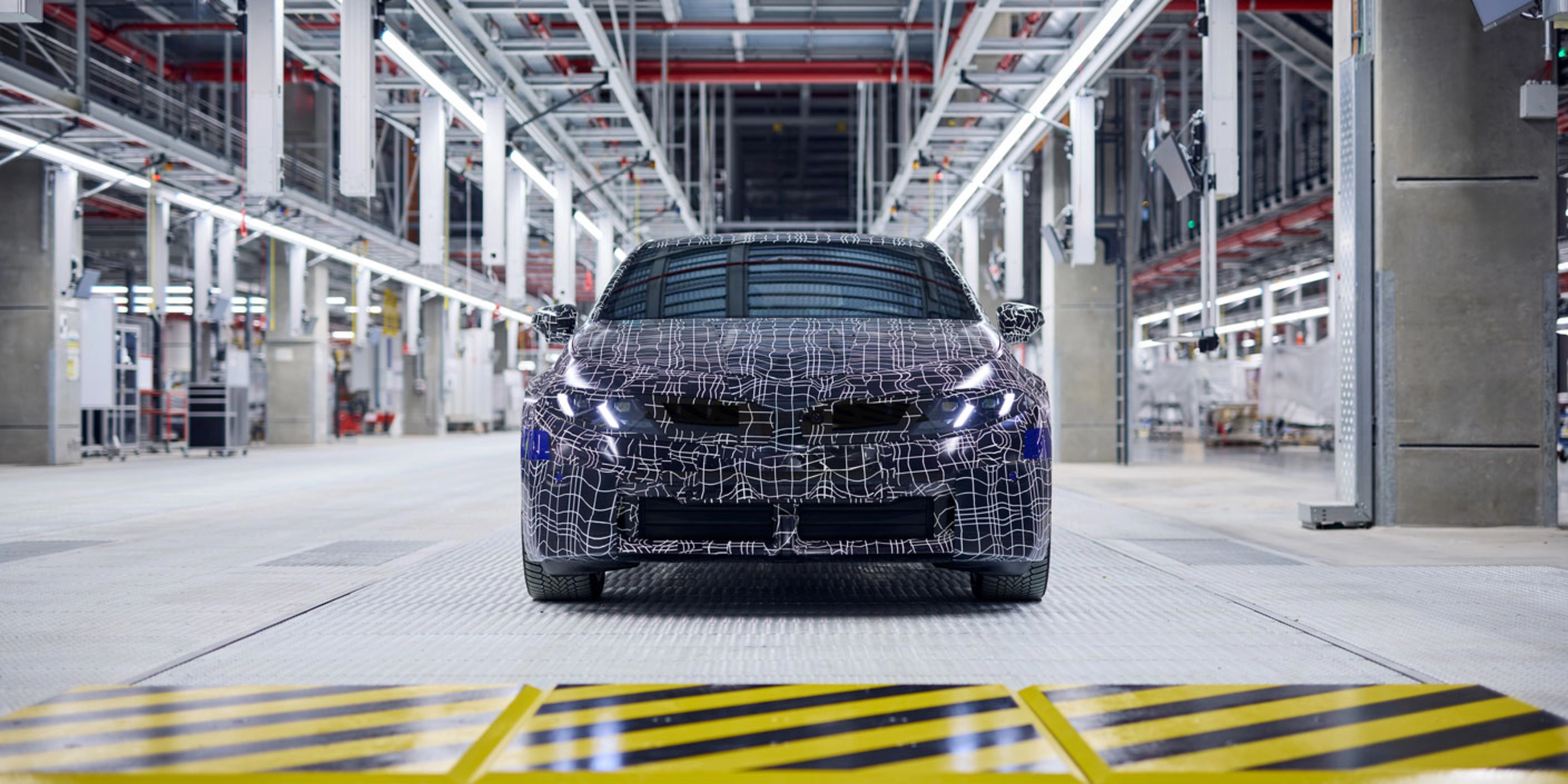 Ein getarntes Auto-Prototyp steht in einer hell beleuchteten Fahrzeugproduktionshalle.