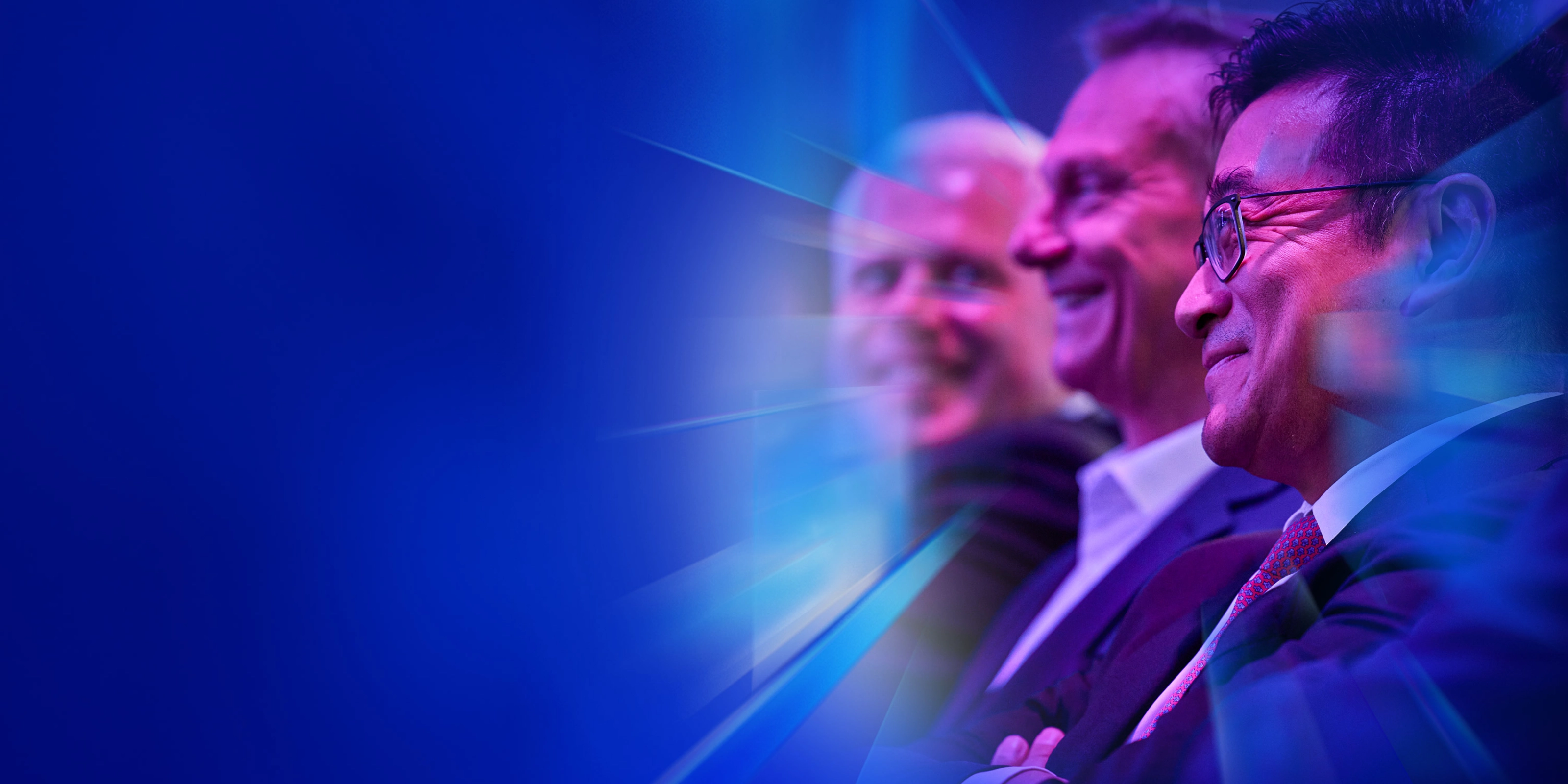Drei lächelnde Männer im Anzug sitzen beim IAA Summit im Publikum.