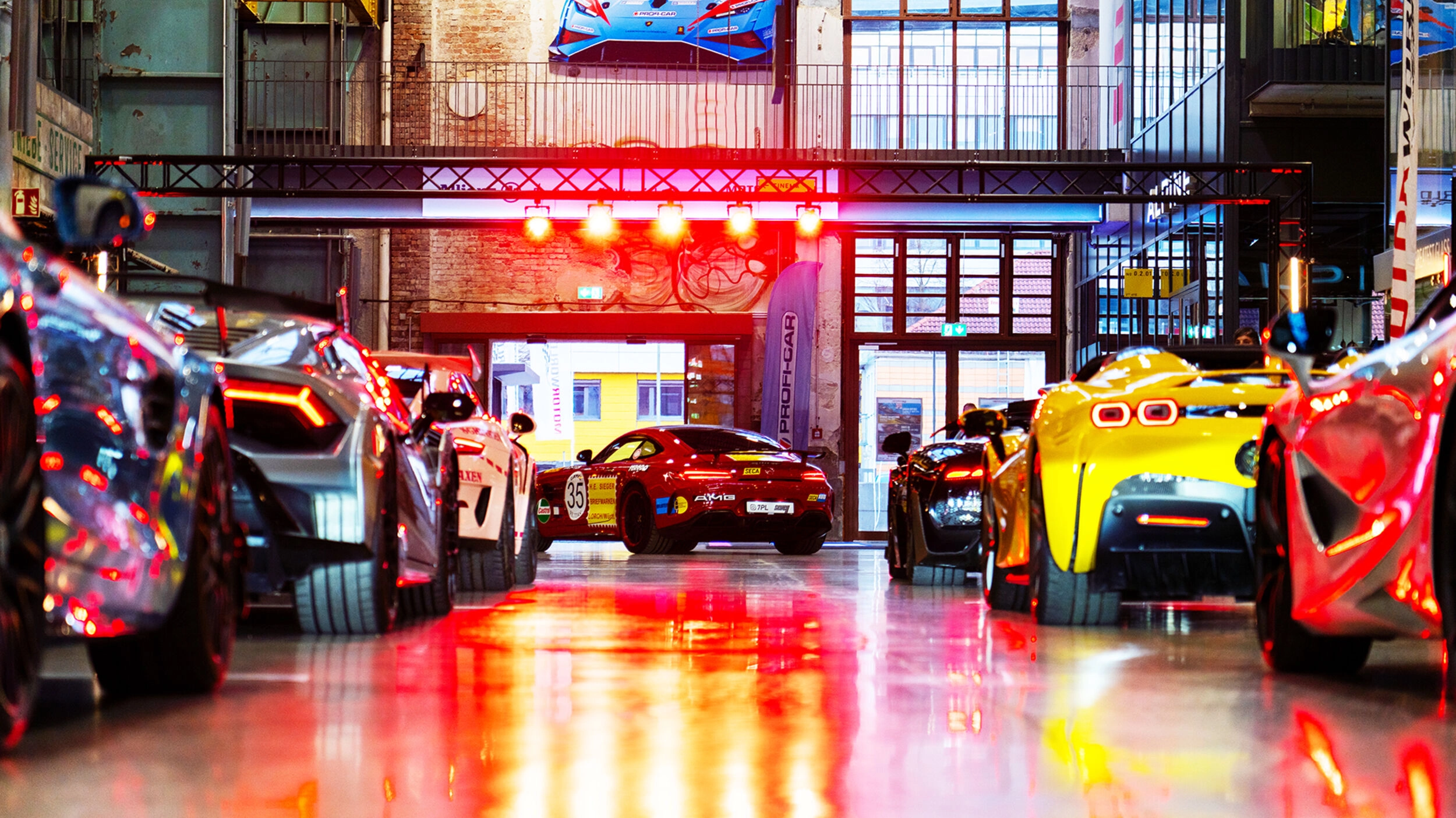 Mehrere Sportwagen stehen in einer hell beleuchteten Industriehalle bei einer Autoausstellung.