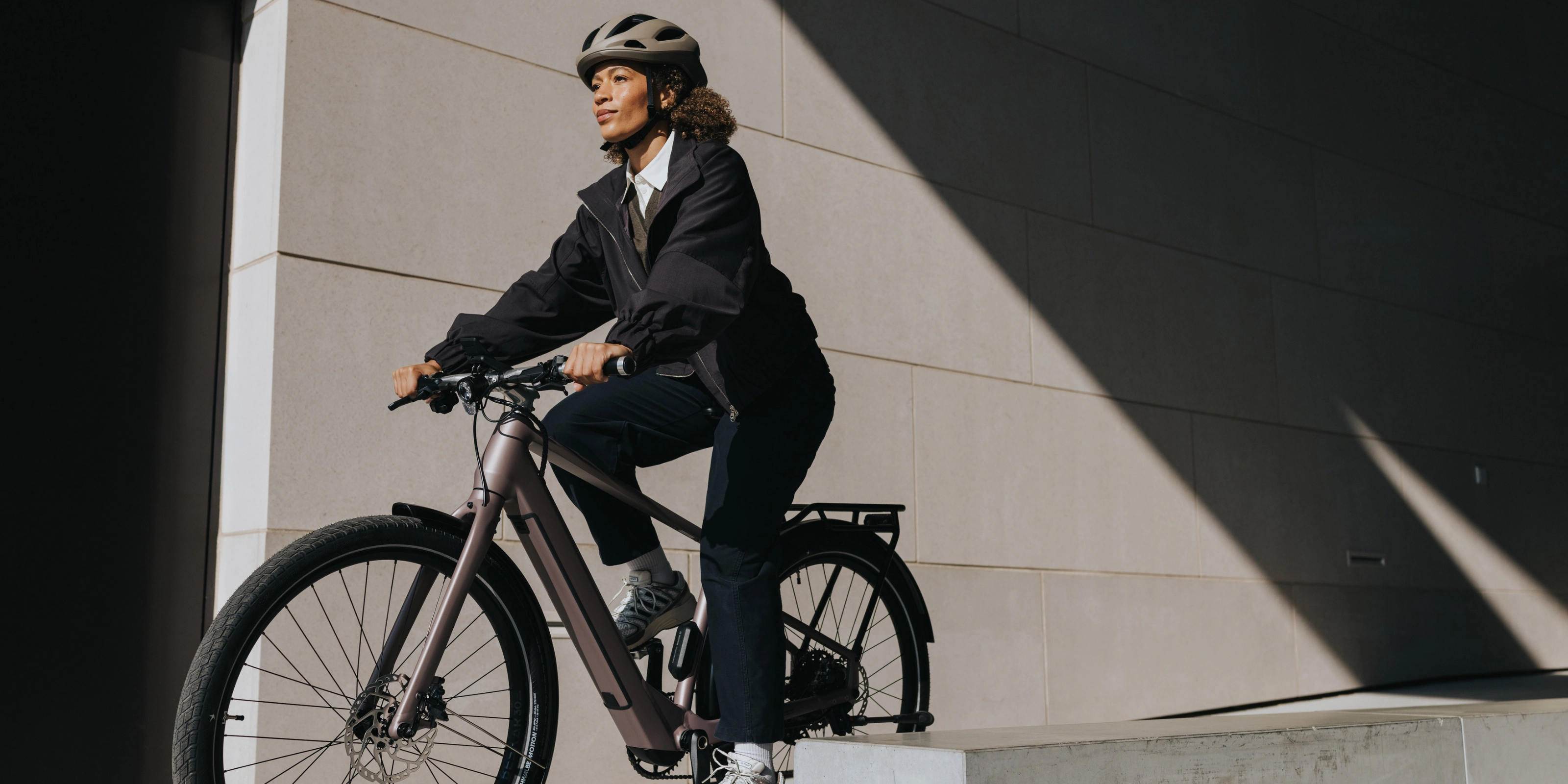 Person mit Helm fährt ein E-Bike neben einem modernen Gebäude.