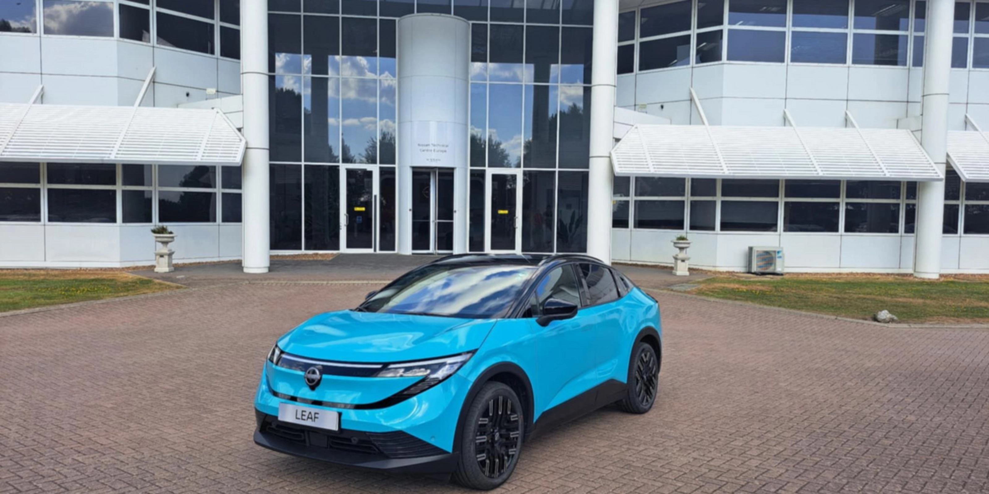 Blauer Nissan Crossover steht vor einem modernen Gebäude mit Glasfassade.