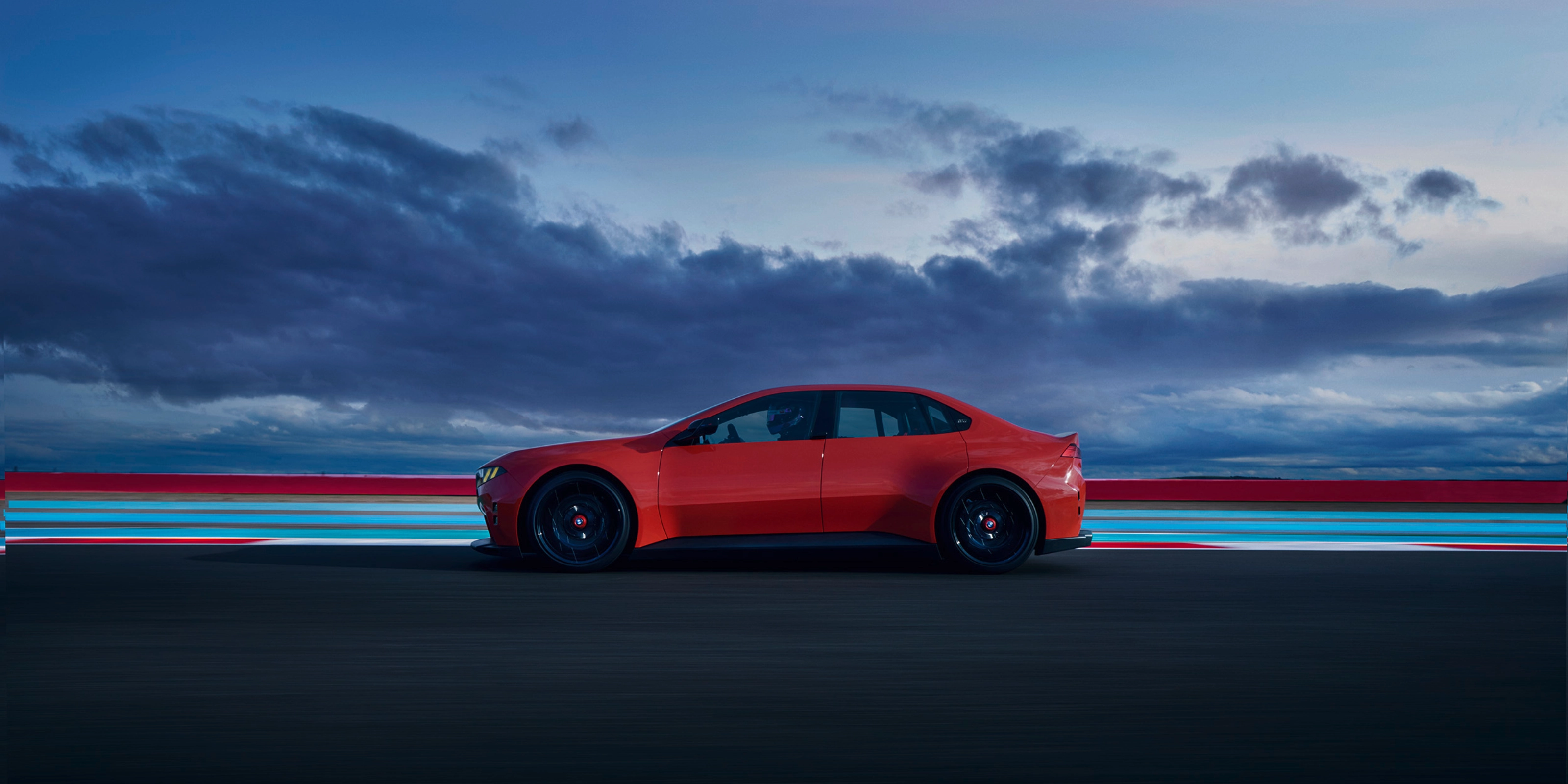 Red car driving on a road at dusk with clouds in the background.