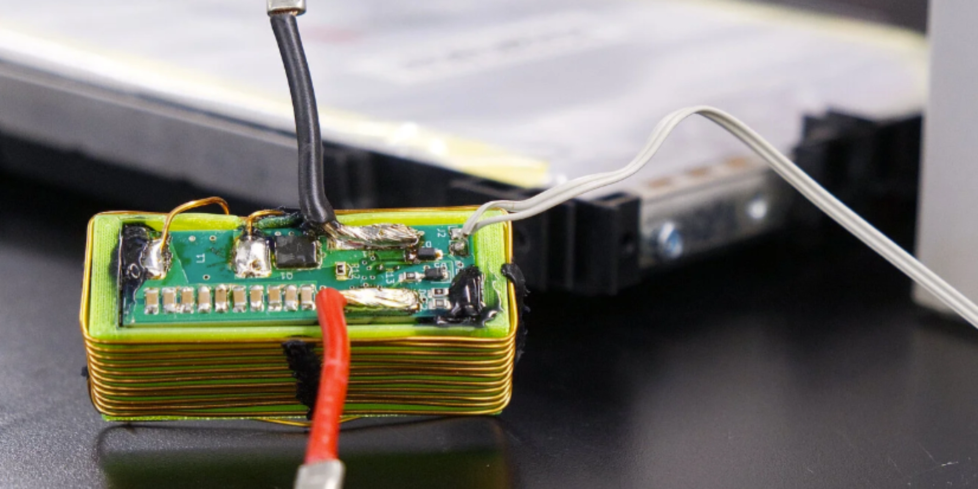 Nahaufnahme eines elektronischen Batteriemoduls mit angeschlossenen Kabeln auf einem Labortisch.