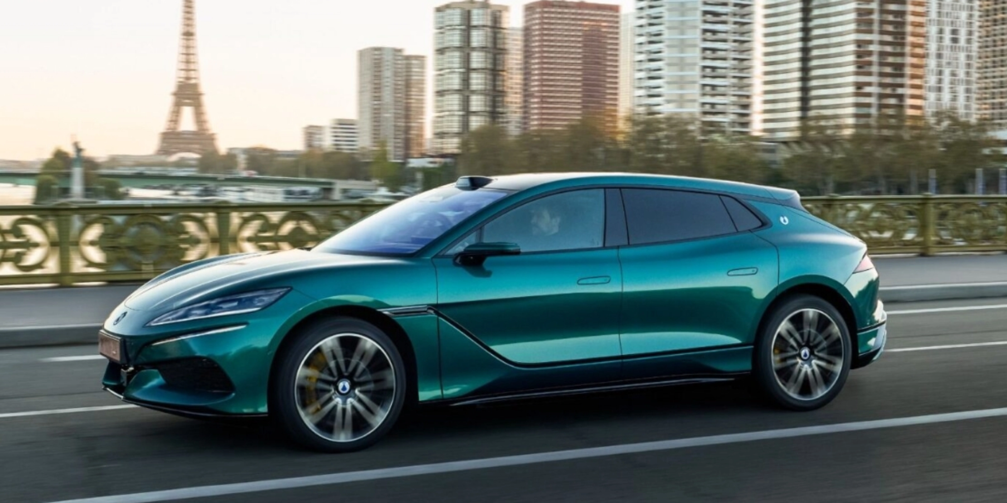 Turquoise BYD electric car driving on a city road with a skyline in the background.