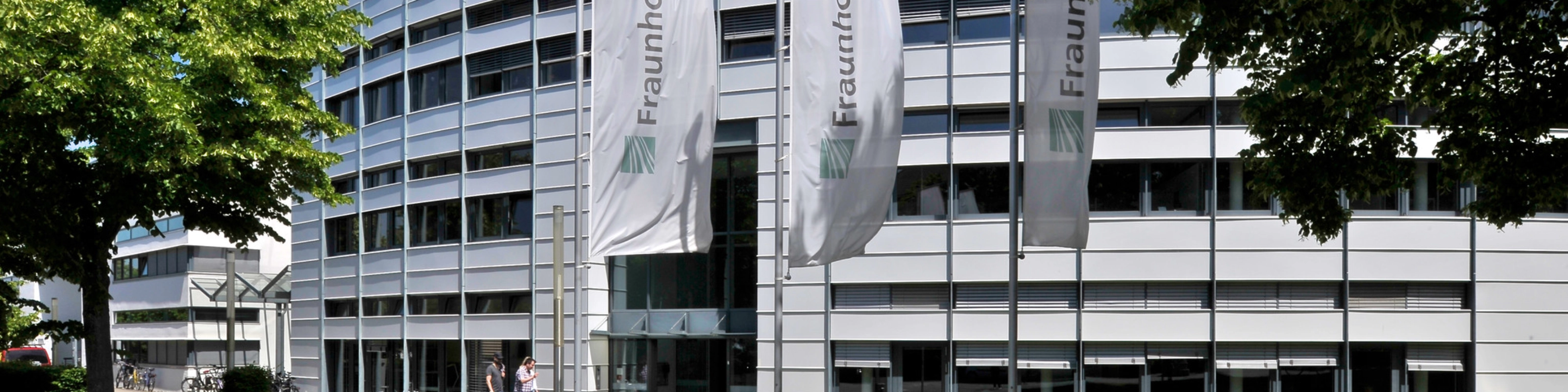 Modernes Fraunhofer-Institutsgebäude mit Fahnen und Bäumen davor.