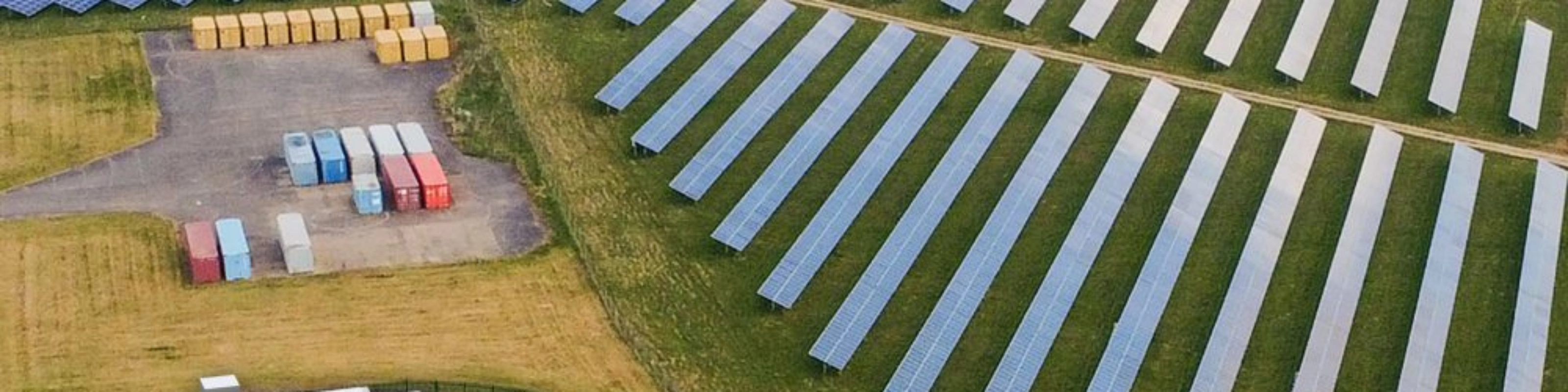 Luftaufnahme einer Solaranlage mit Reihen von Solarpaneelen und mehreren Containern.