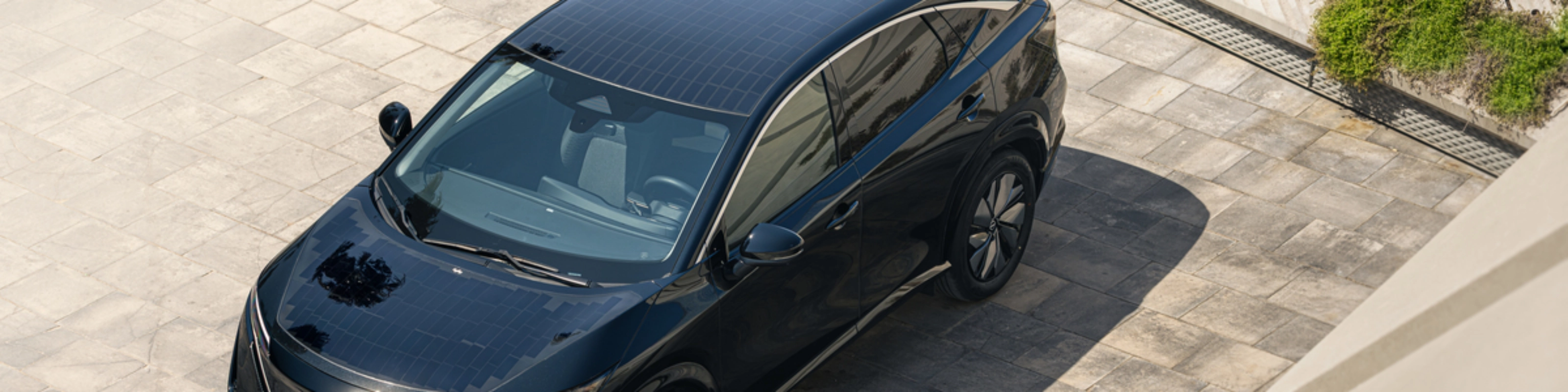 Ein schwarzes Elektro-SUV von Nissan steht auf einer gepflasterten Fläche im Sonnenlicht.