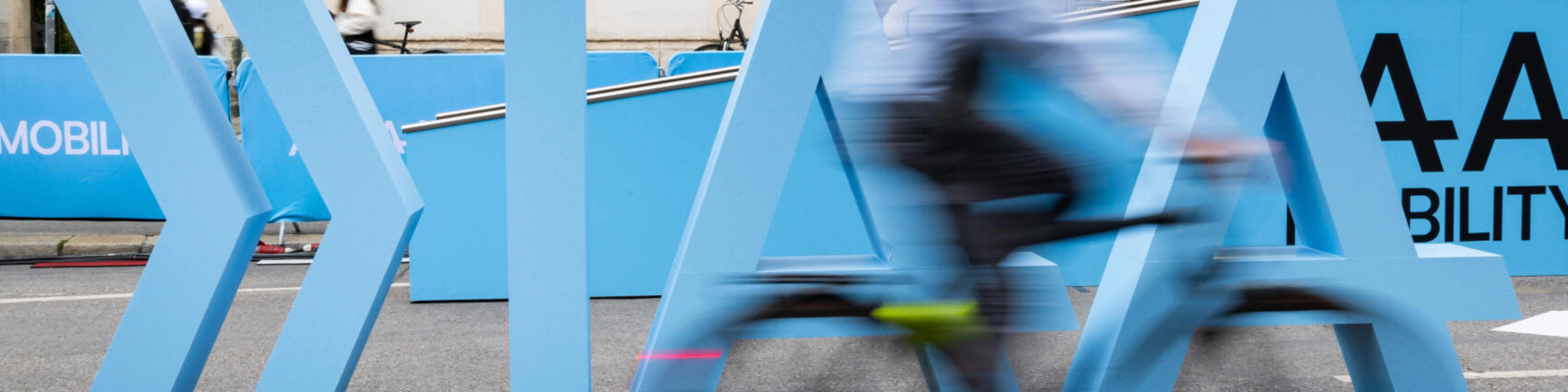 Cyclist rides past large IAA Mobility lettering on a city street.