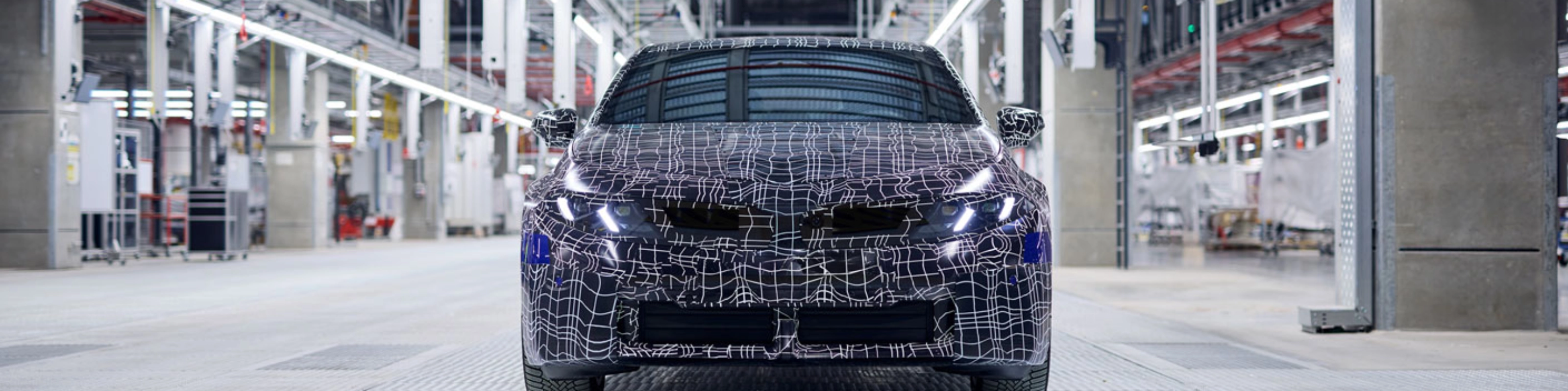 Ein getarntes Auto-Prototyp steht in einer hell beleuchteten Fahrzeugproduktionshalle.