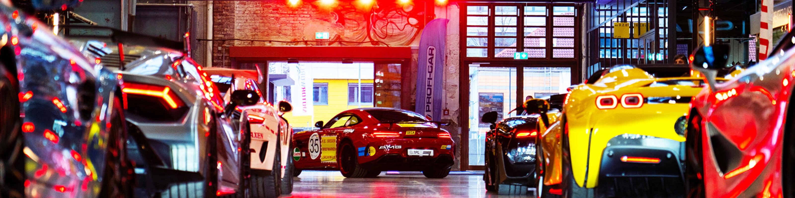 Mehrere Sportwagen stehen in einer hell beleuchteten Industriehalle bei einer Autoausstellung.