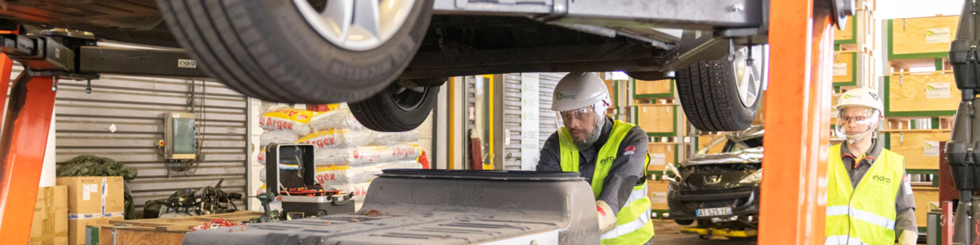 Worker in factory handling EV battery module under vehicle lift.