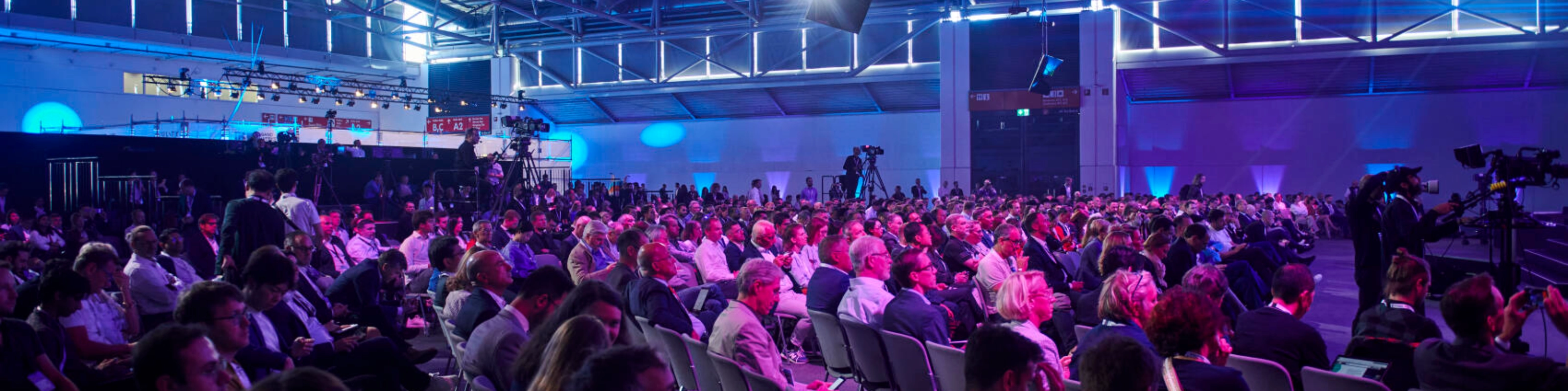 Großes Publikum in einem Konferenzsaal bei der IAA MOBILITY mit Bühnenlicht und Kameras.