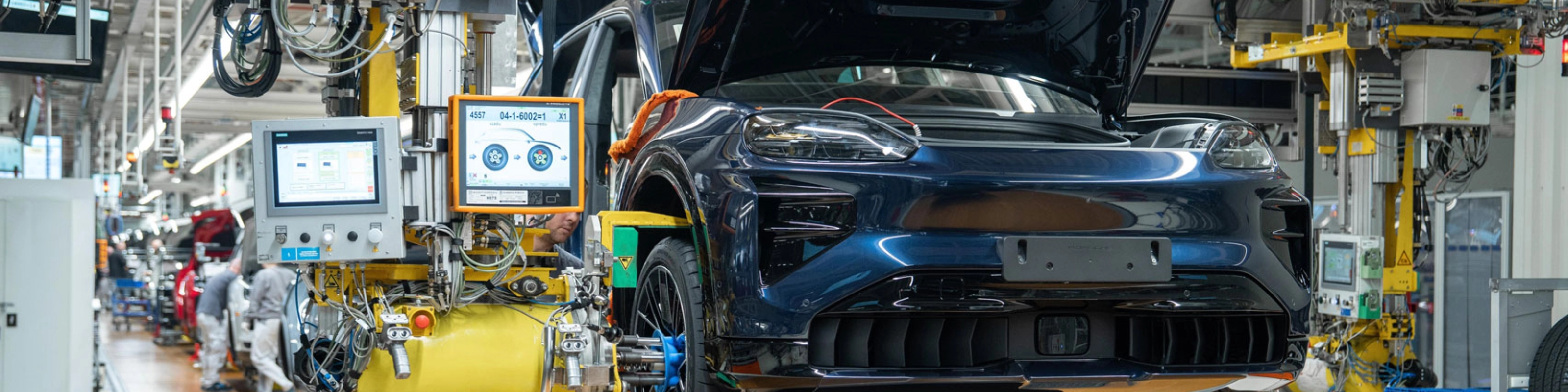 Teilmontiertes Elektroauto auf dem Montageband mit offenem Kofferraum und Maschinen ringsum.