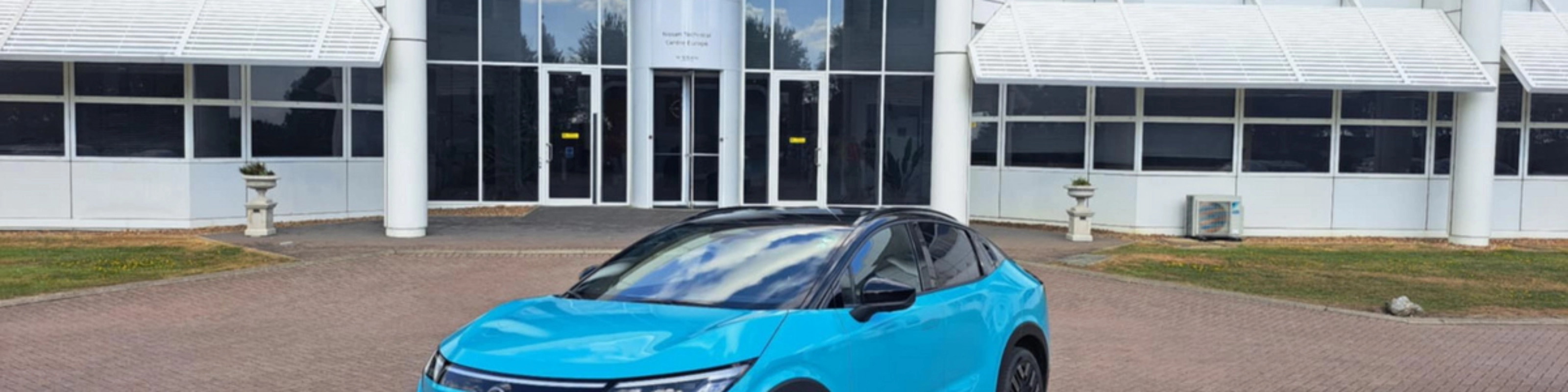 Blauer Nissan Crossover steht vor einem modernen Gebäude mit Glasfassade.