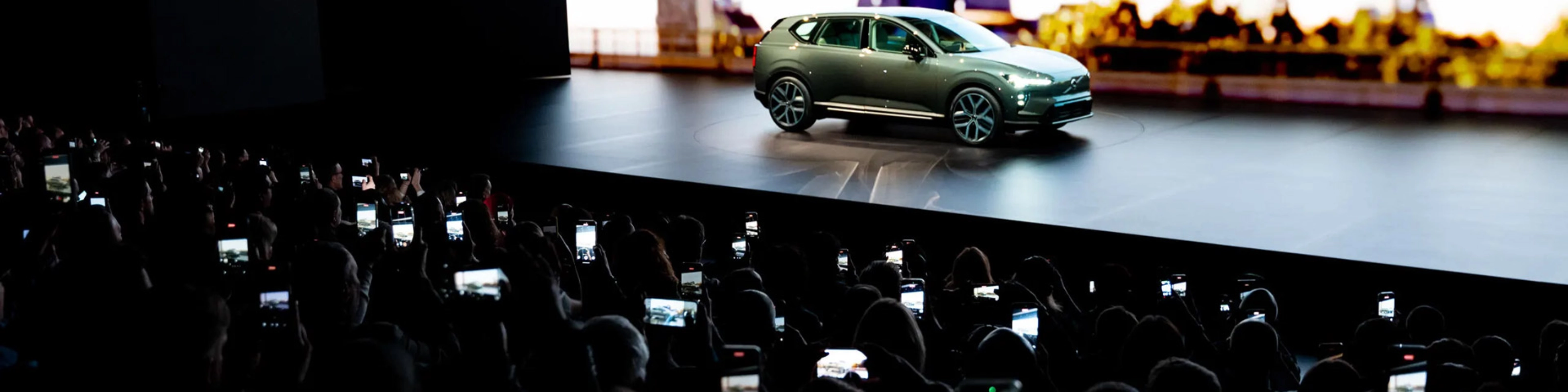 Elektrischer SUV wird auf einer Bühne präsentiert, das Publikum fotografiert mit Smartphones.