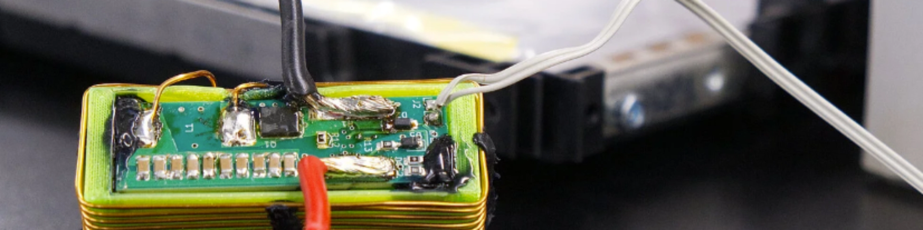 Nahaufnahme eines elektronischen Batteriemoduls mit angeschlossenen Kabeln auf einem Labortisch.