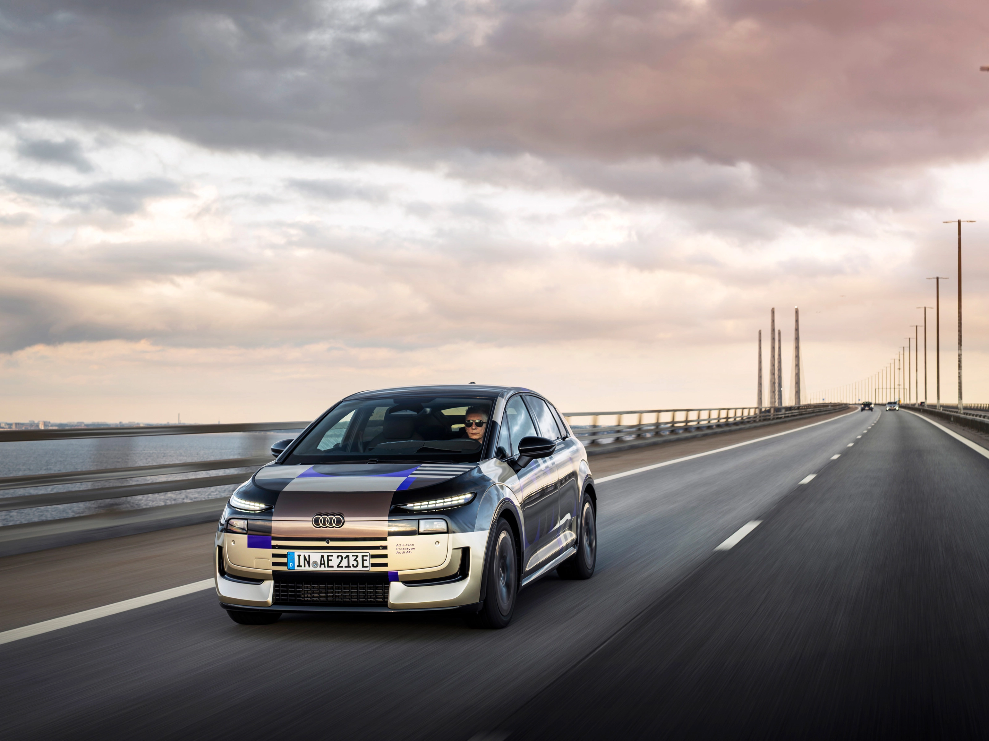 Audi prototype electric vehicle driving on an open road at sunset.