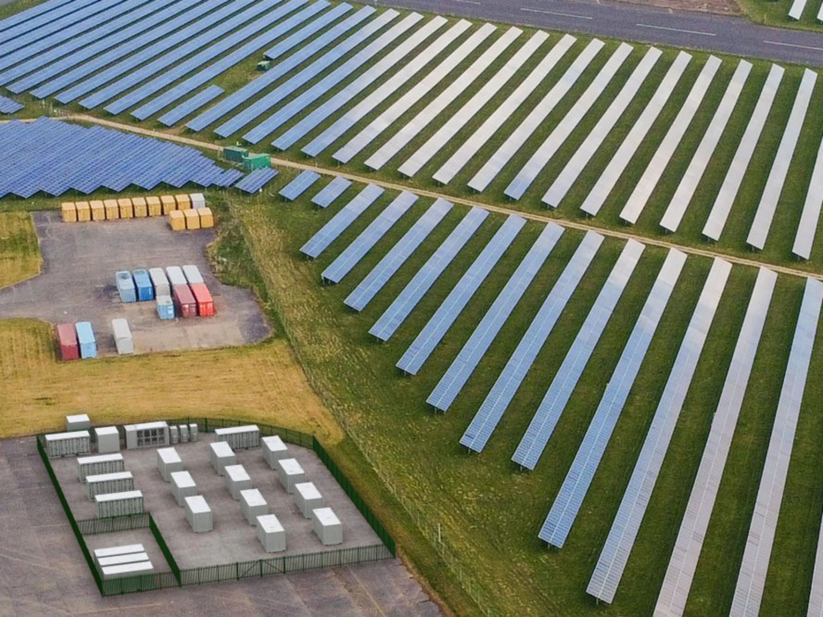 Luftaufnahme einer Solaranlage mit Reihen von Solarpaneelen und mehreren Containern.