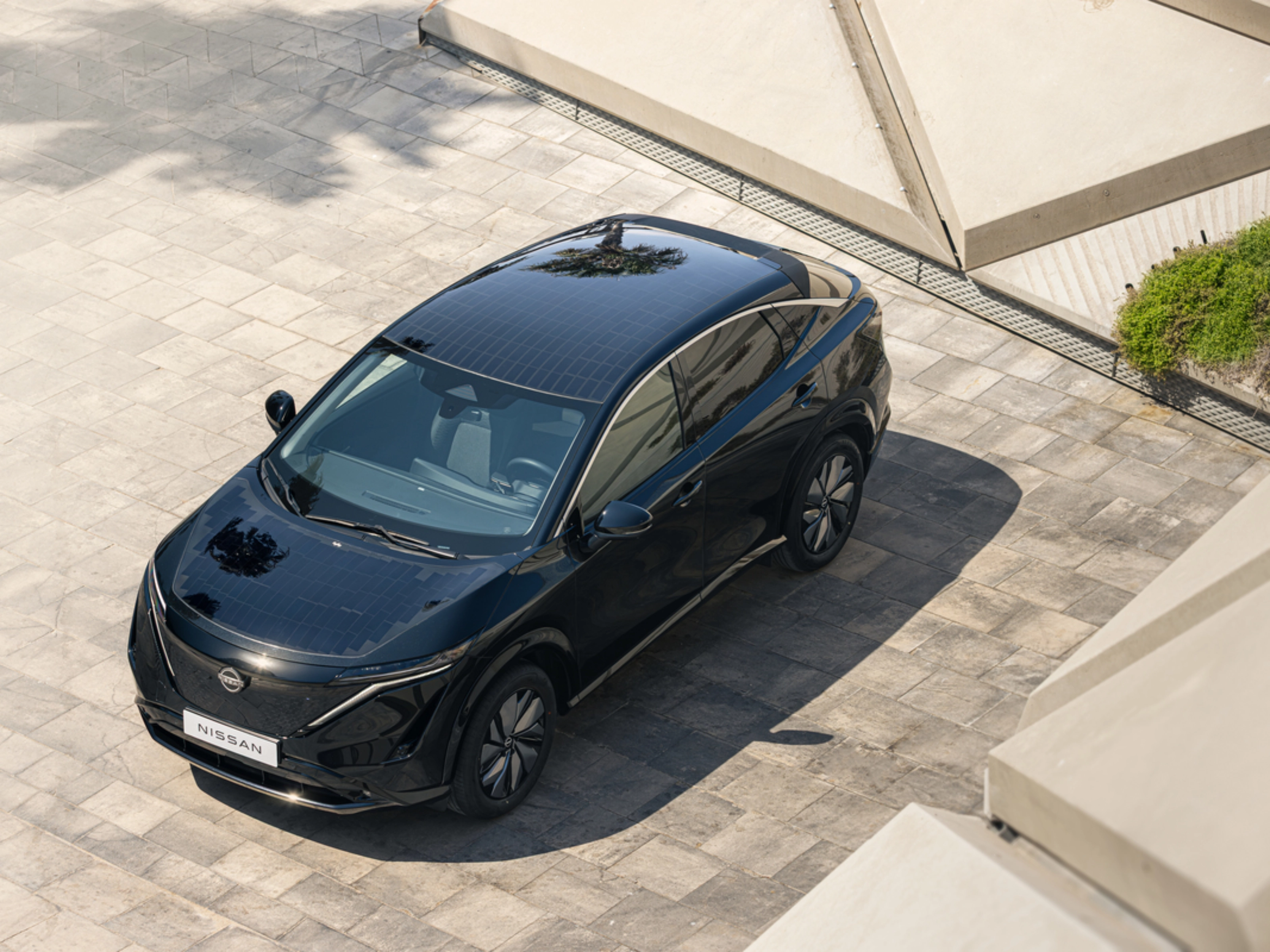 Ein schwarzes Elektro-SUV von Nissan steht auf einer gepflasterten Fläche im Sonnenlicht.