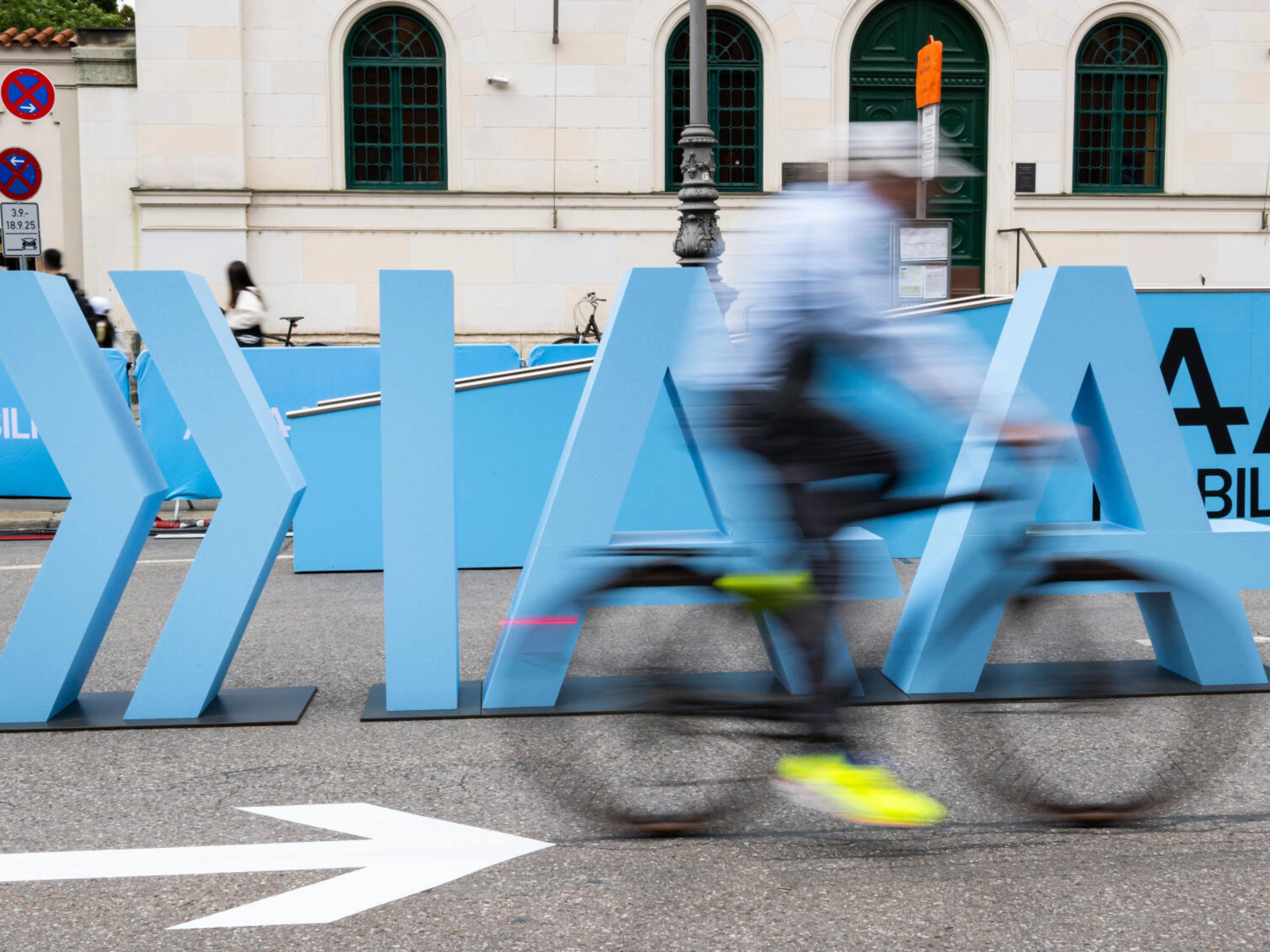 Cyclist rides past large IAA Mobility lettering on a city street.