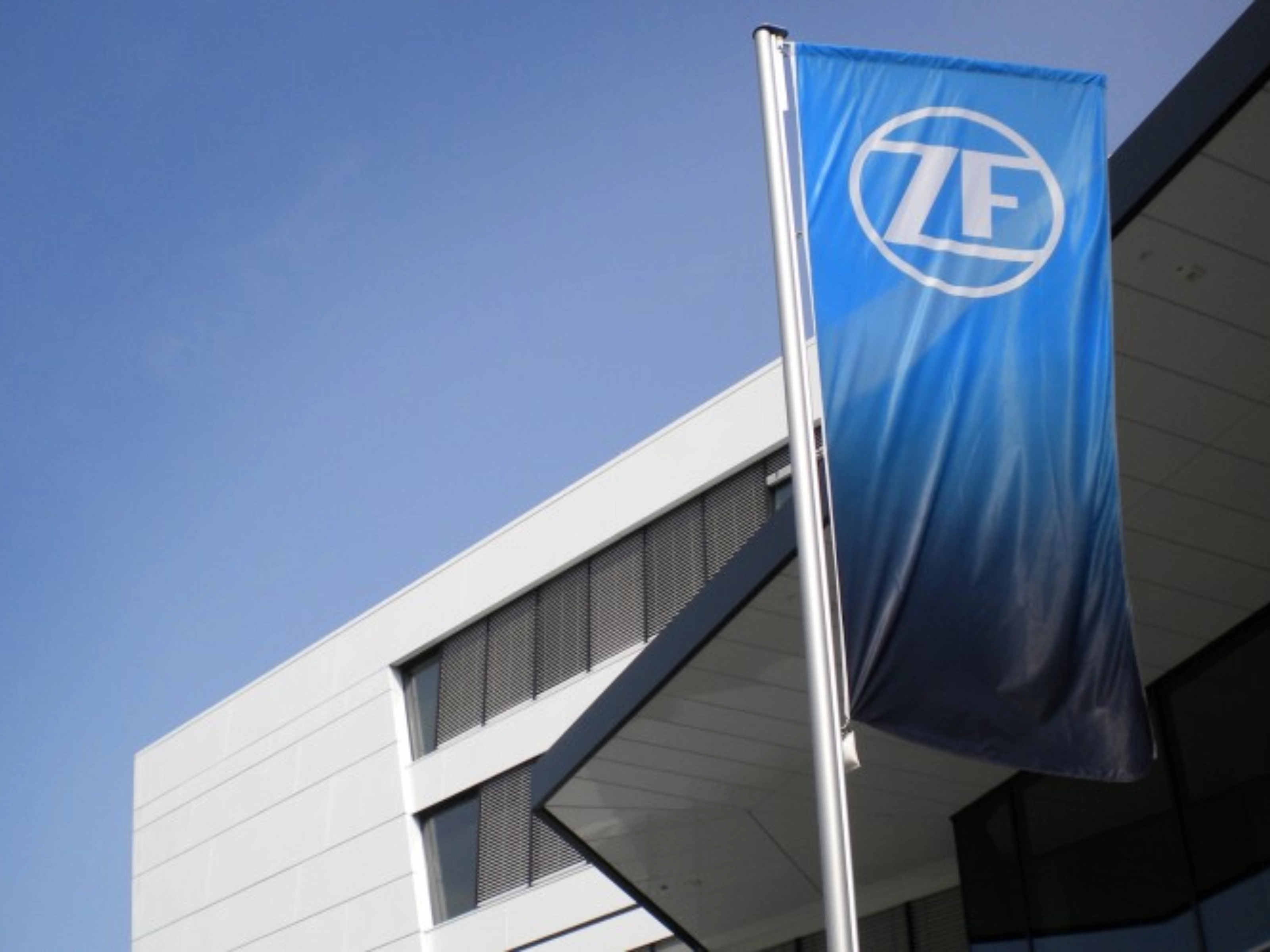 Blaue ZF-Flagge vor einem modernen Bürogebäude mit weißer Fassade.