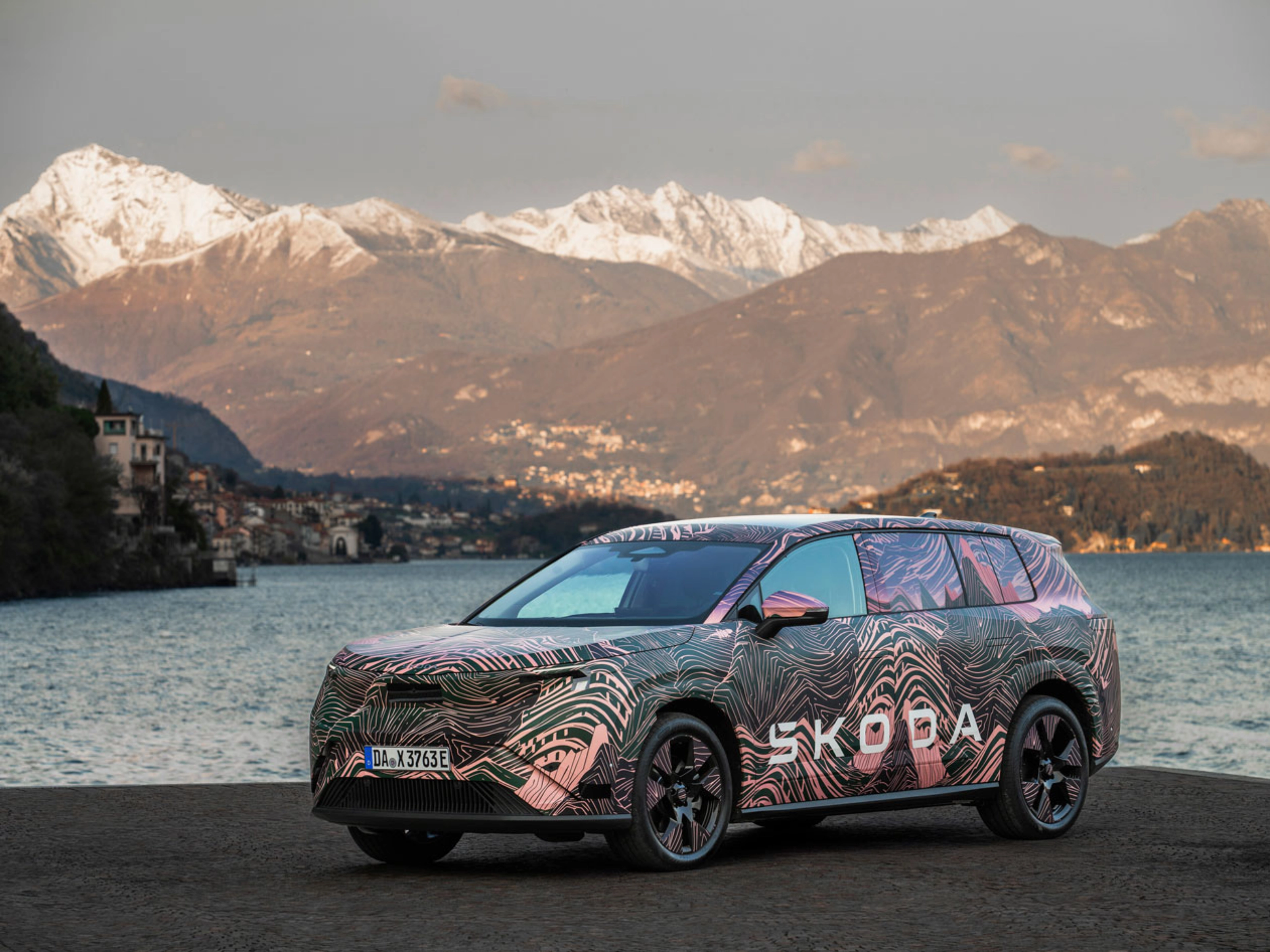 Getarnter Škoda steht am See vor schneebedeckten Bergen.